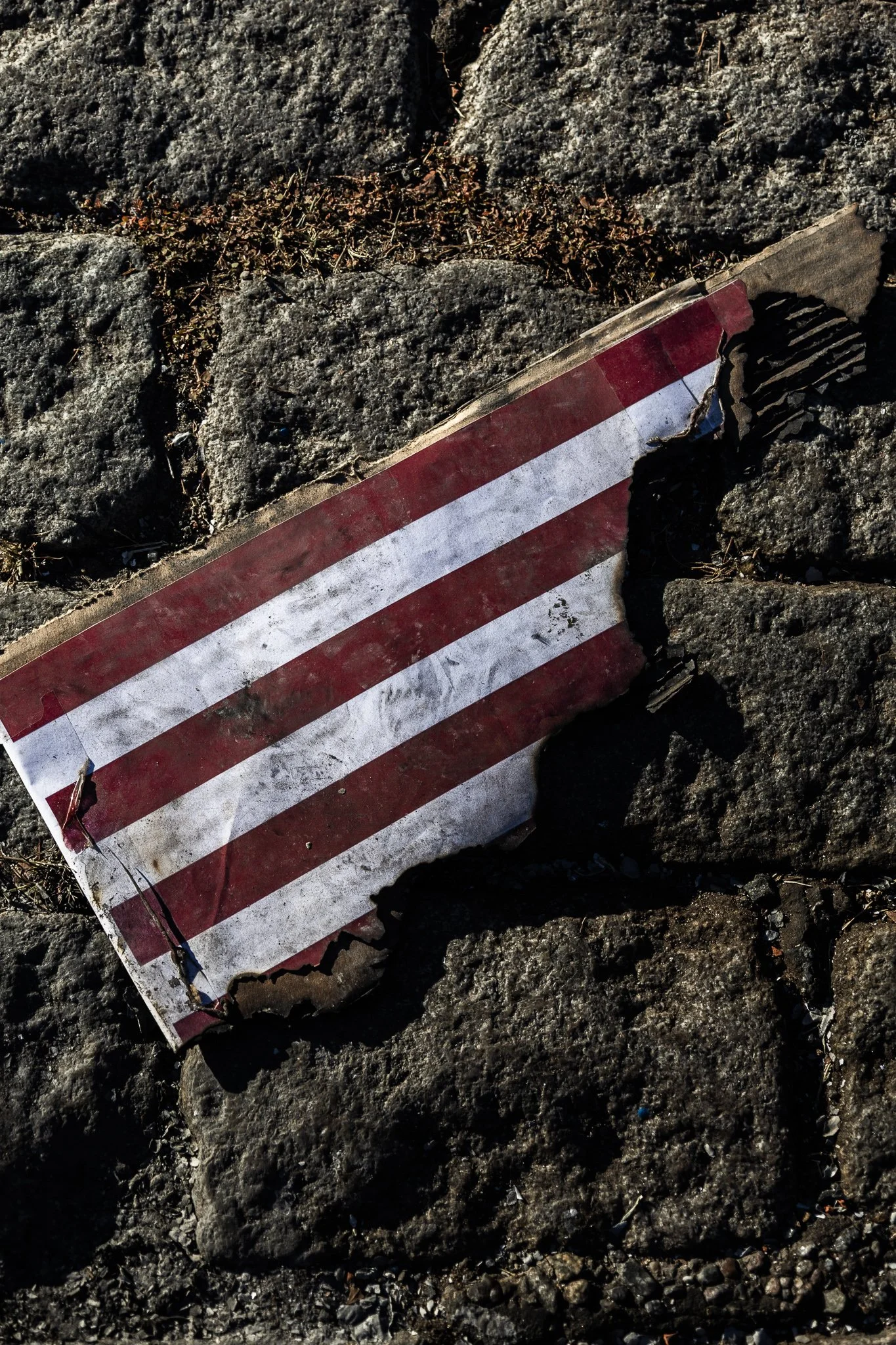 Señal de tránsito rota y caída en el suelo, en un camino de piedras.