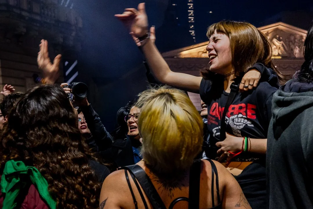 Un grupo de personas celebrando y disfrutando en la calle, con una mujer en el centro levantando la mano y otras personas sonriendo y tomándose fotos.