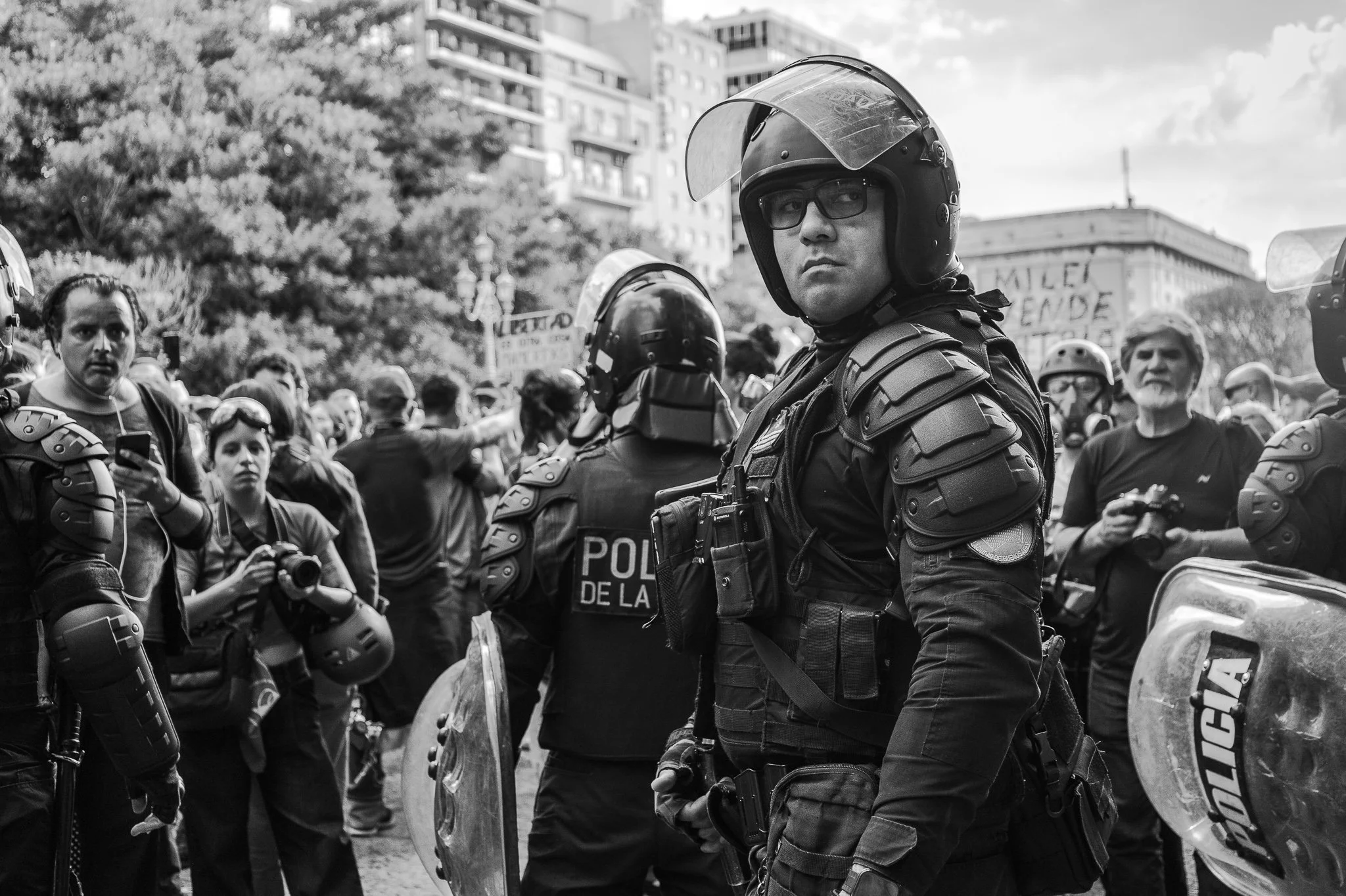 Policías con equipo antimotines enfrentan a una multitud en una protesta urbana, algunos llevan escudos y cascos.