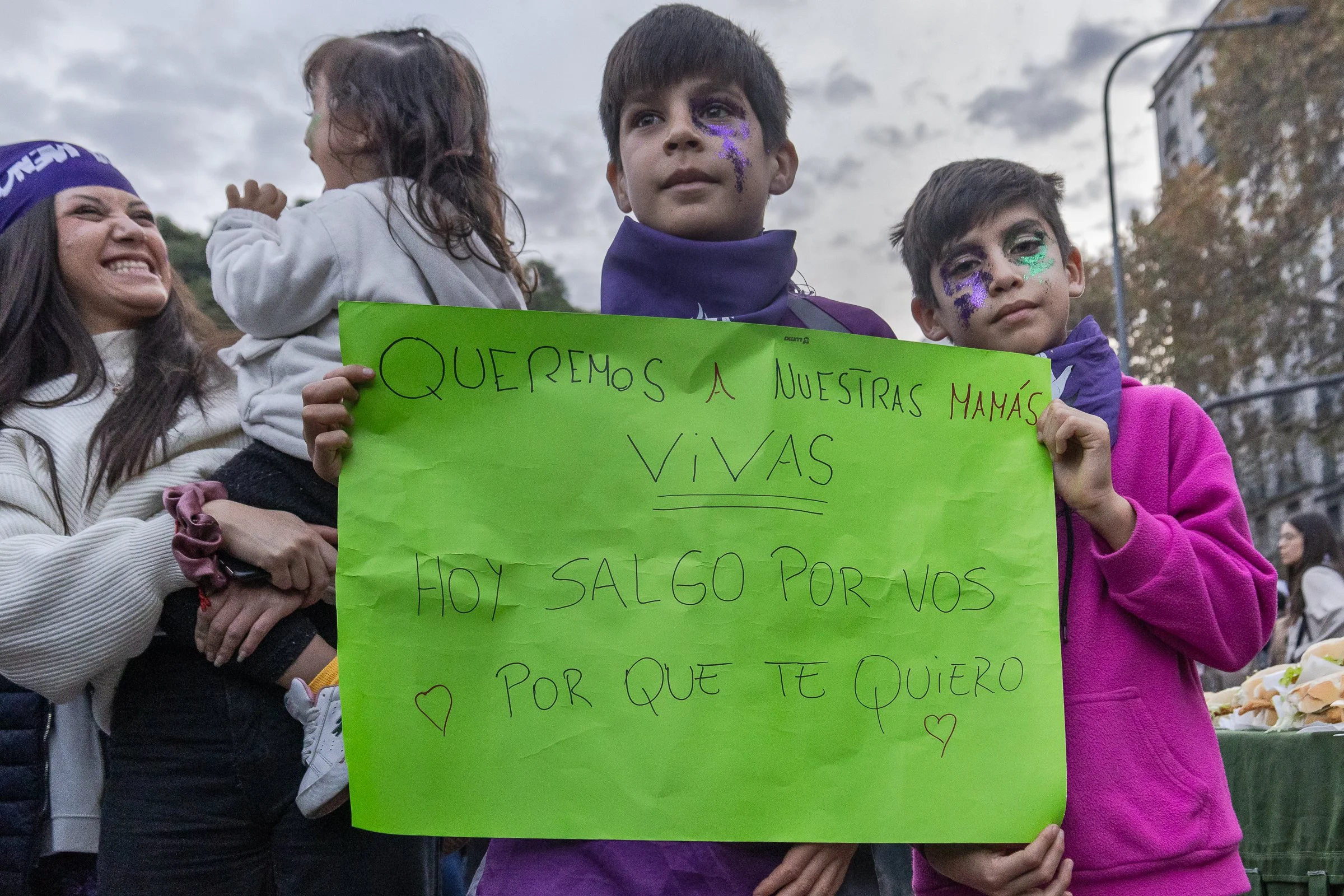 Niños y niñas en una manifestación sosteniendo carteles, con pintura en la cara y ropa de colores violeta y verde. 