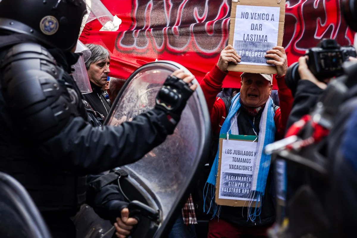 Manifestante con cartel que dice 'No vengo a dar lastima, sí respeto', en medio de policías con escudos, en una protesta.