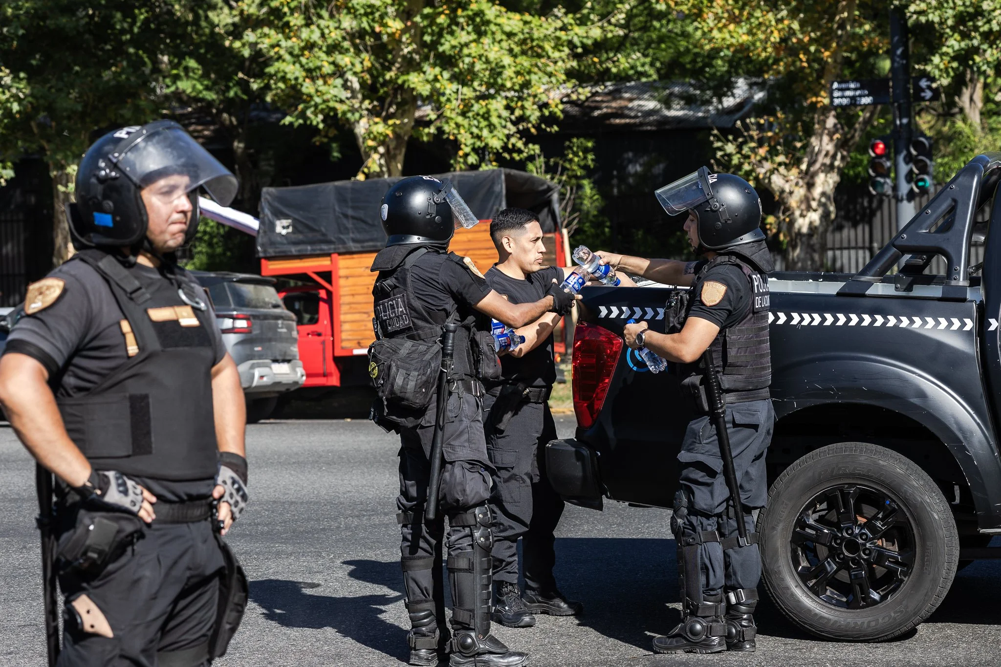 Un grupo de policías antidisturbios se encuentra en una calle, algunos de ellos están conversando, mientras uno de ellos ofrece agua a un hombre.