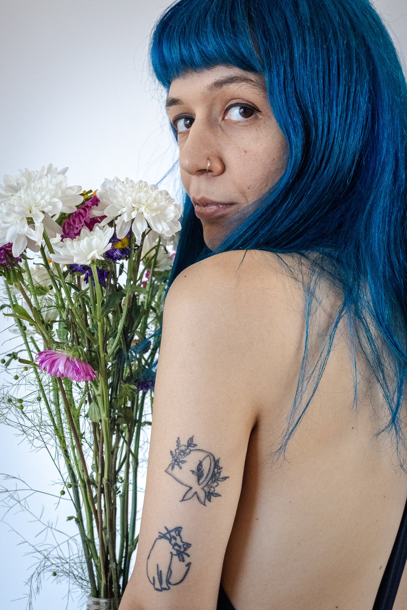 Fotografía digital del rostro de una mujer de espaldas, con cabello de color azul y sosteniendo un ramo de flores