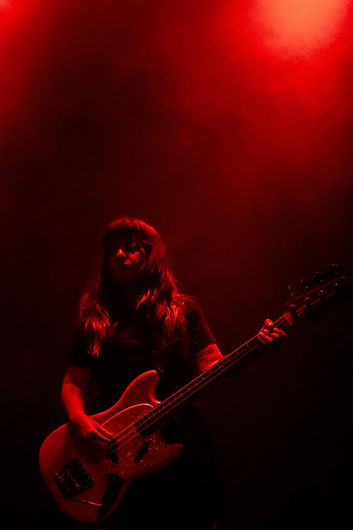 Mujer tocando la guitarra en un escenario con iluminación roja.