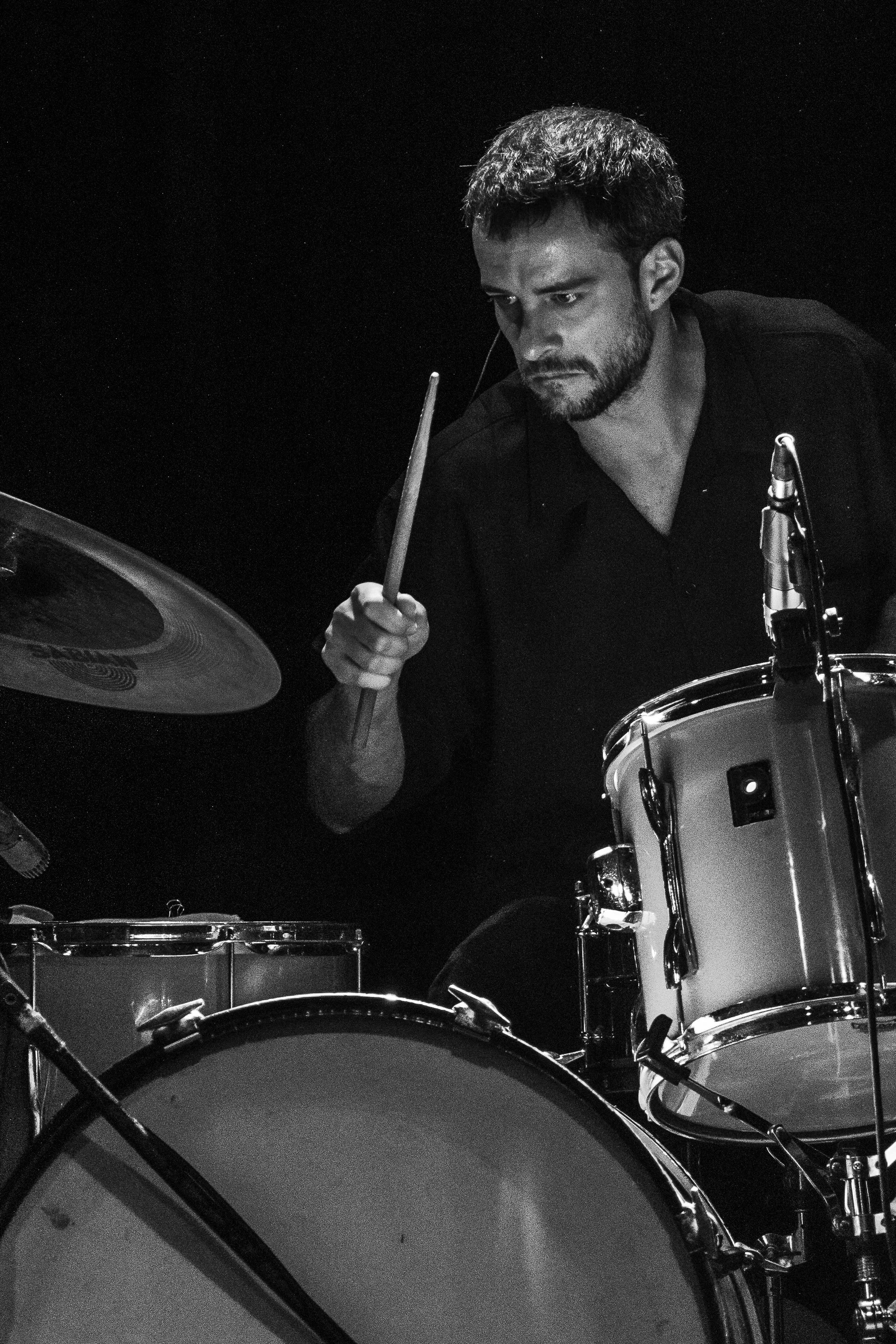 Un hombre tocando la batería en un escenario, en blanco y negro.