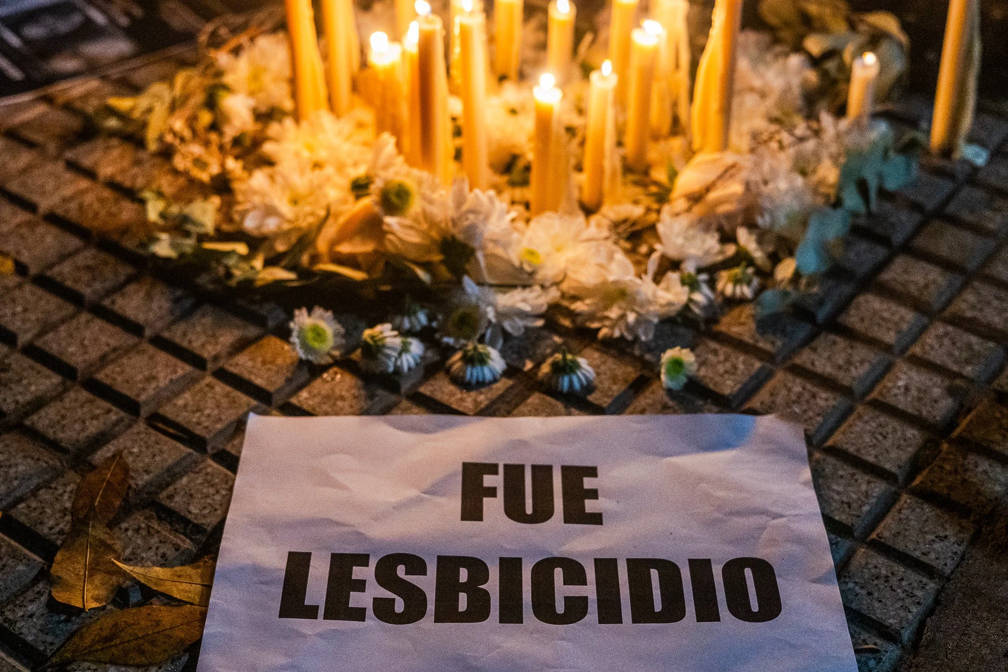 Velas encendidas y flores en un altar, con un letrero que dice 'FUE LESBICIDIO'.
