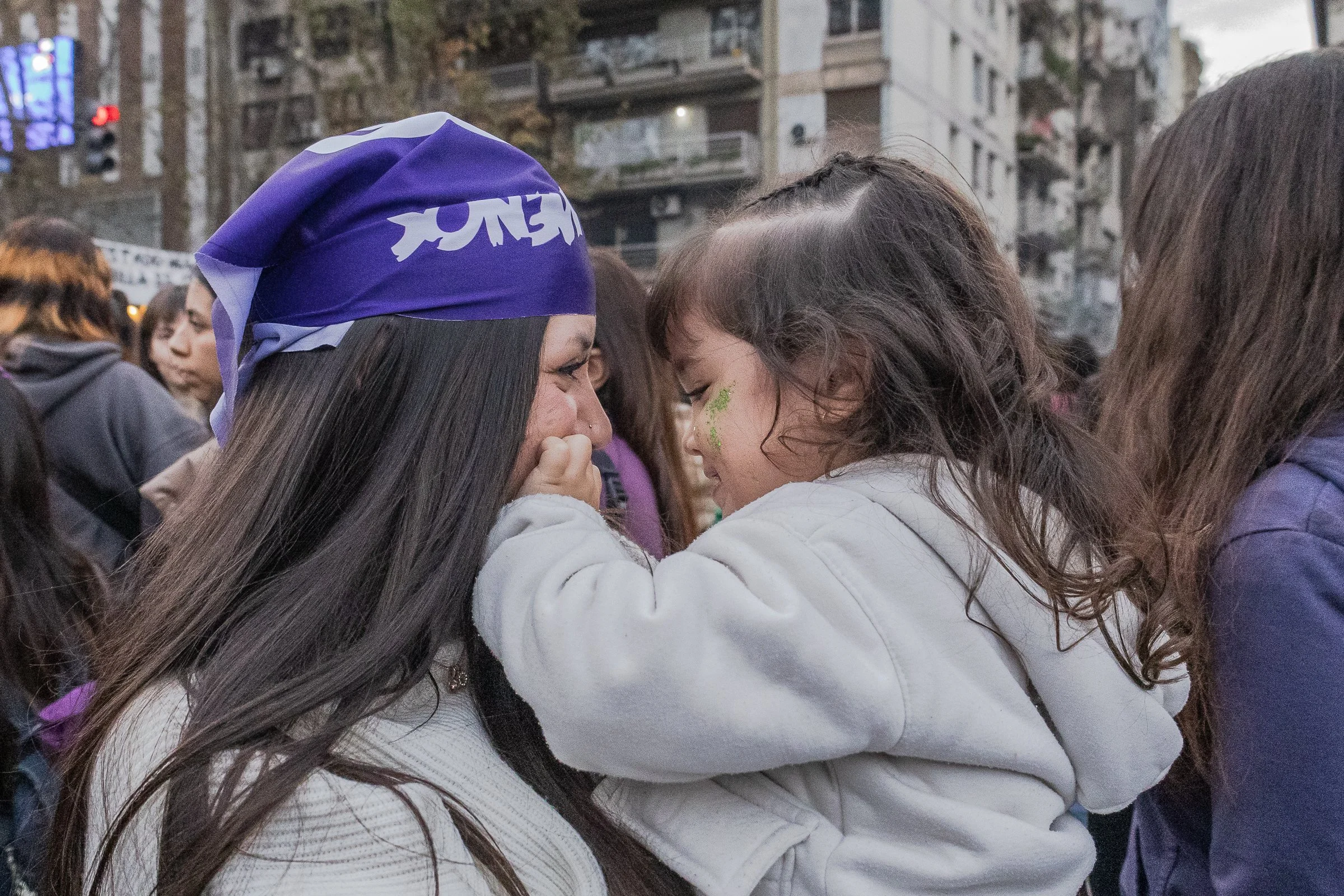 Una madre y su niña sonriendo con la frente juntas en la calle.