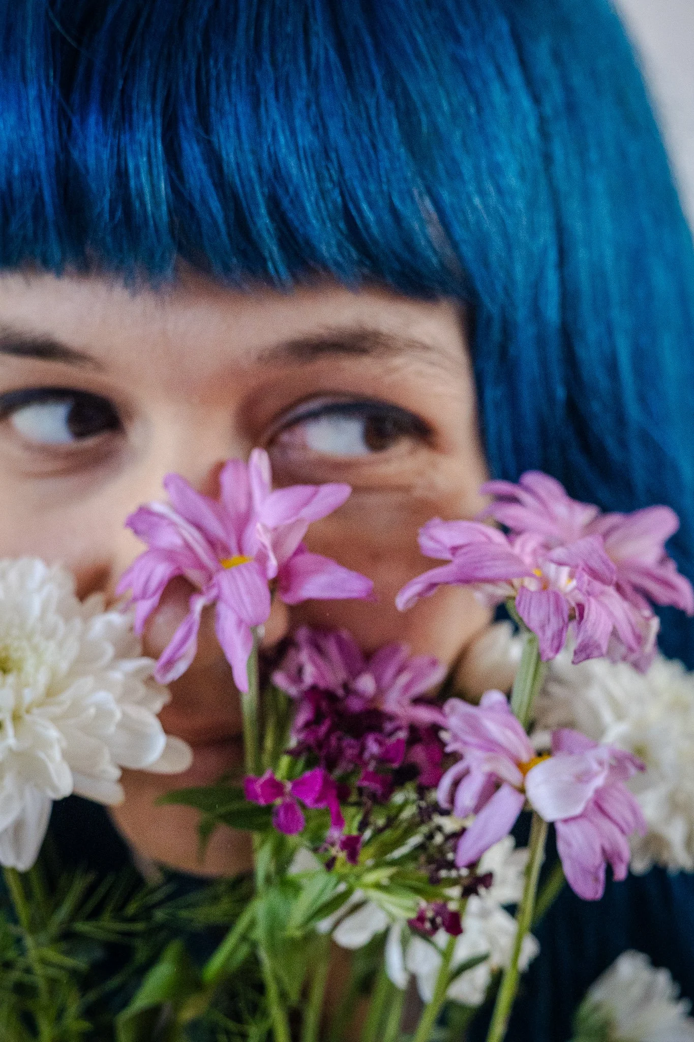 Joven con cabello azul sosteniendo un ramo de flores que cubre parcialmente su rostro.