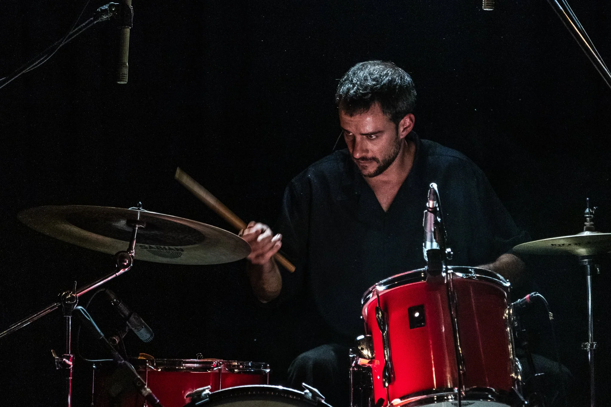 Hombre tocando la batería en un escenario oscuro.