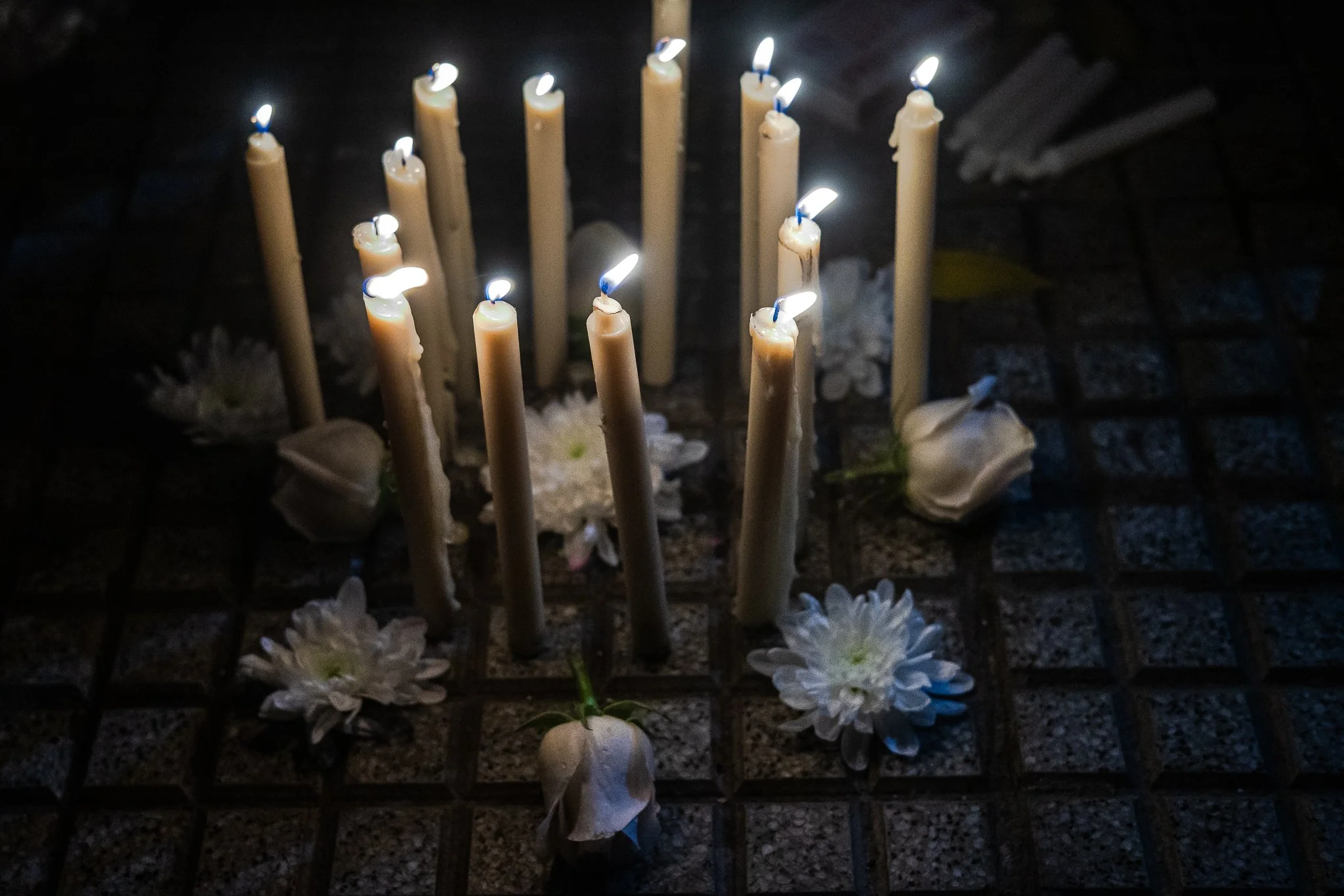 Vela encendida en un entorno oscuro, rodeada de flores blancas.