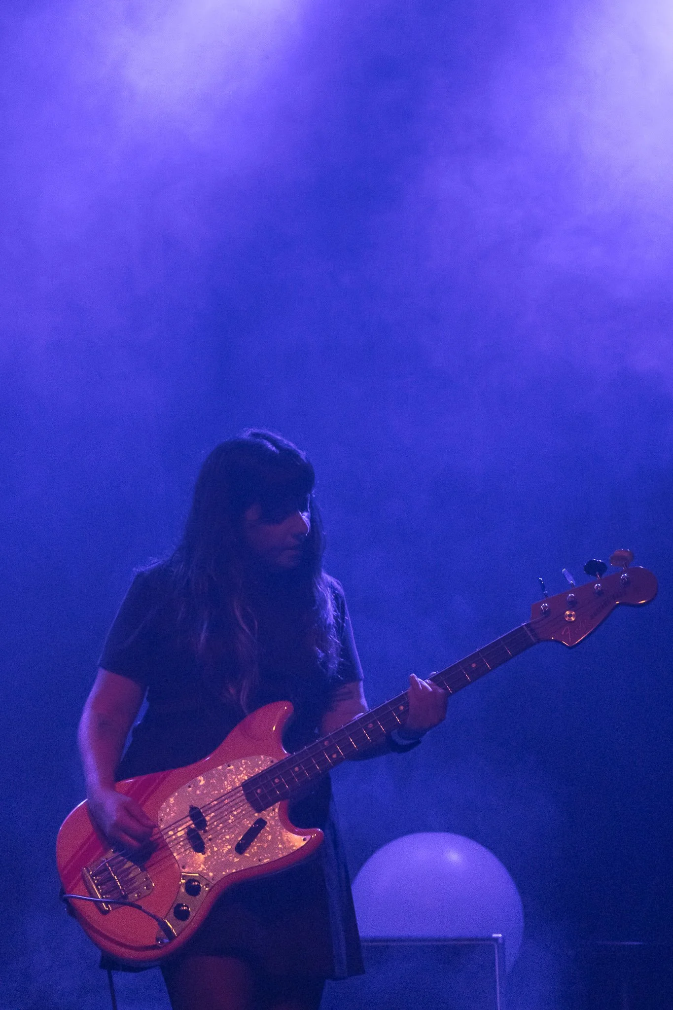 Mujer tocando guitarra eléctrica en un escenario con iluminación morada.
