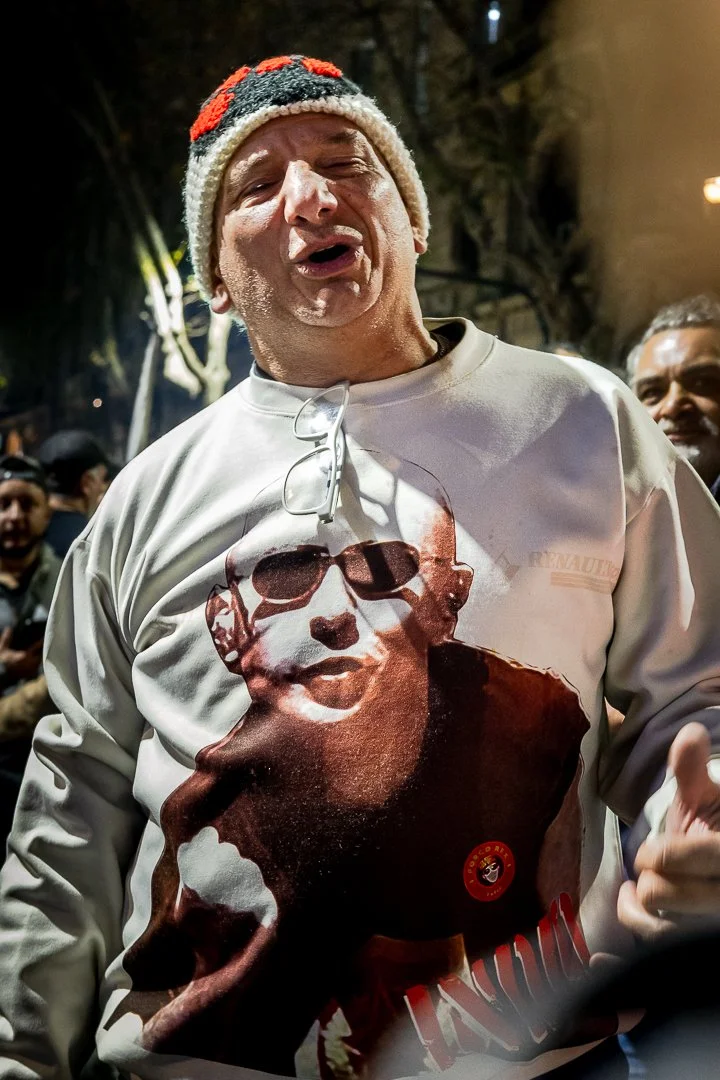 Hombre con gorro de invierno, remera con la imagen del Indio Solari: con muchas personas en el fondo.