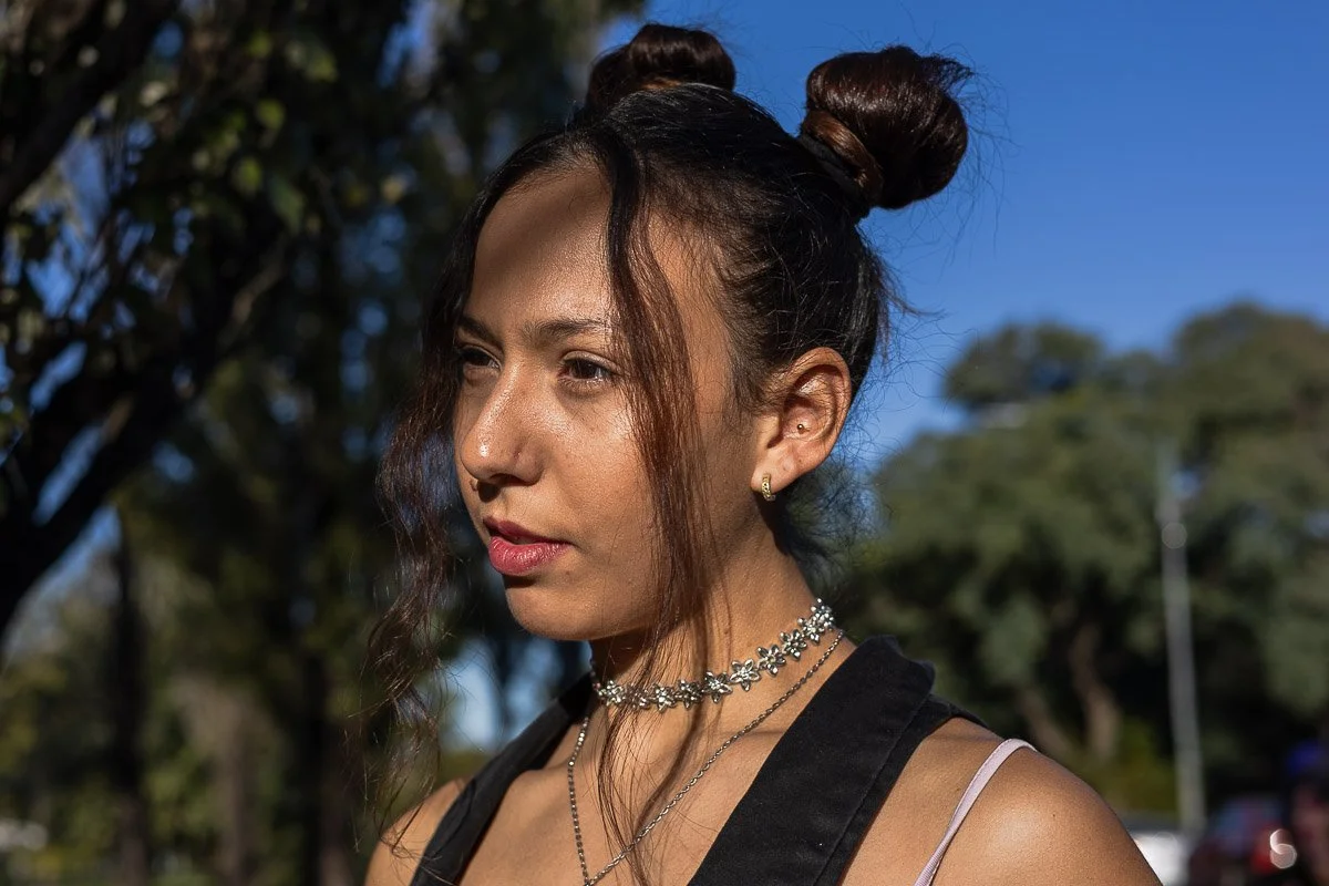 Joven mujer con doble moño en el cabello, usando collar y pendientes, al aire libre en un día soleado.