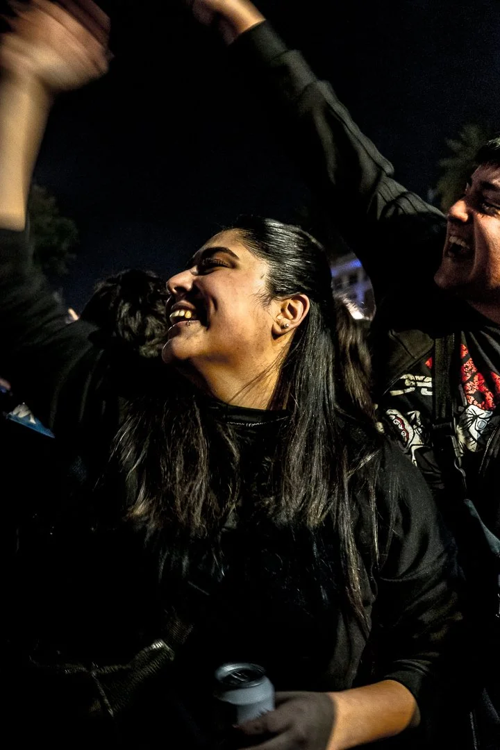 Jóvenes felices en una celebración nocturna, una mujer sonriendo con la lengua afuera y una lata en la mano, acompañada por un hombre que también sonríe.