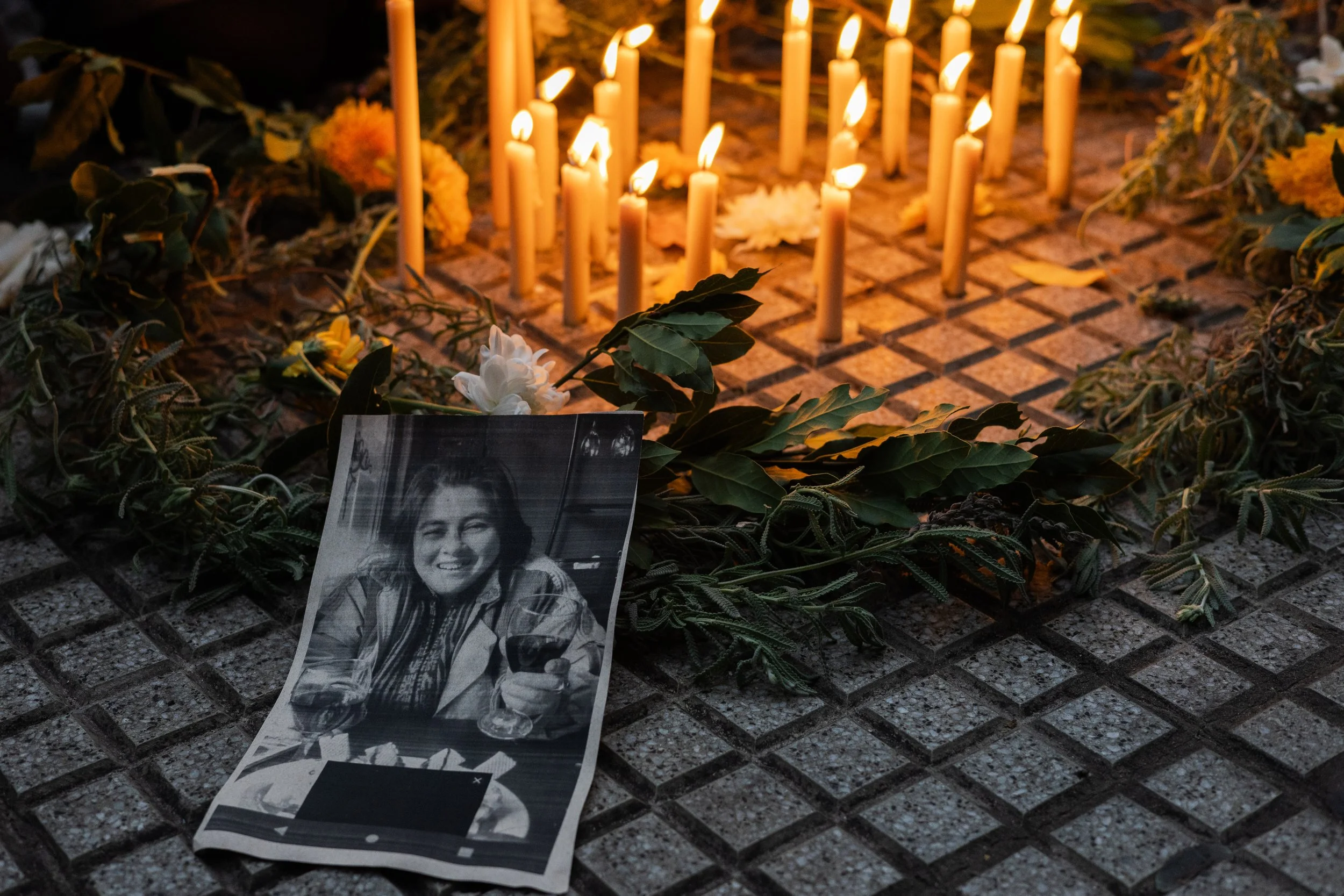 Velas encendidas, flores y una fotografía en blanco y negro de una mujer en un altar conmemorativo.