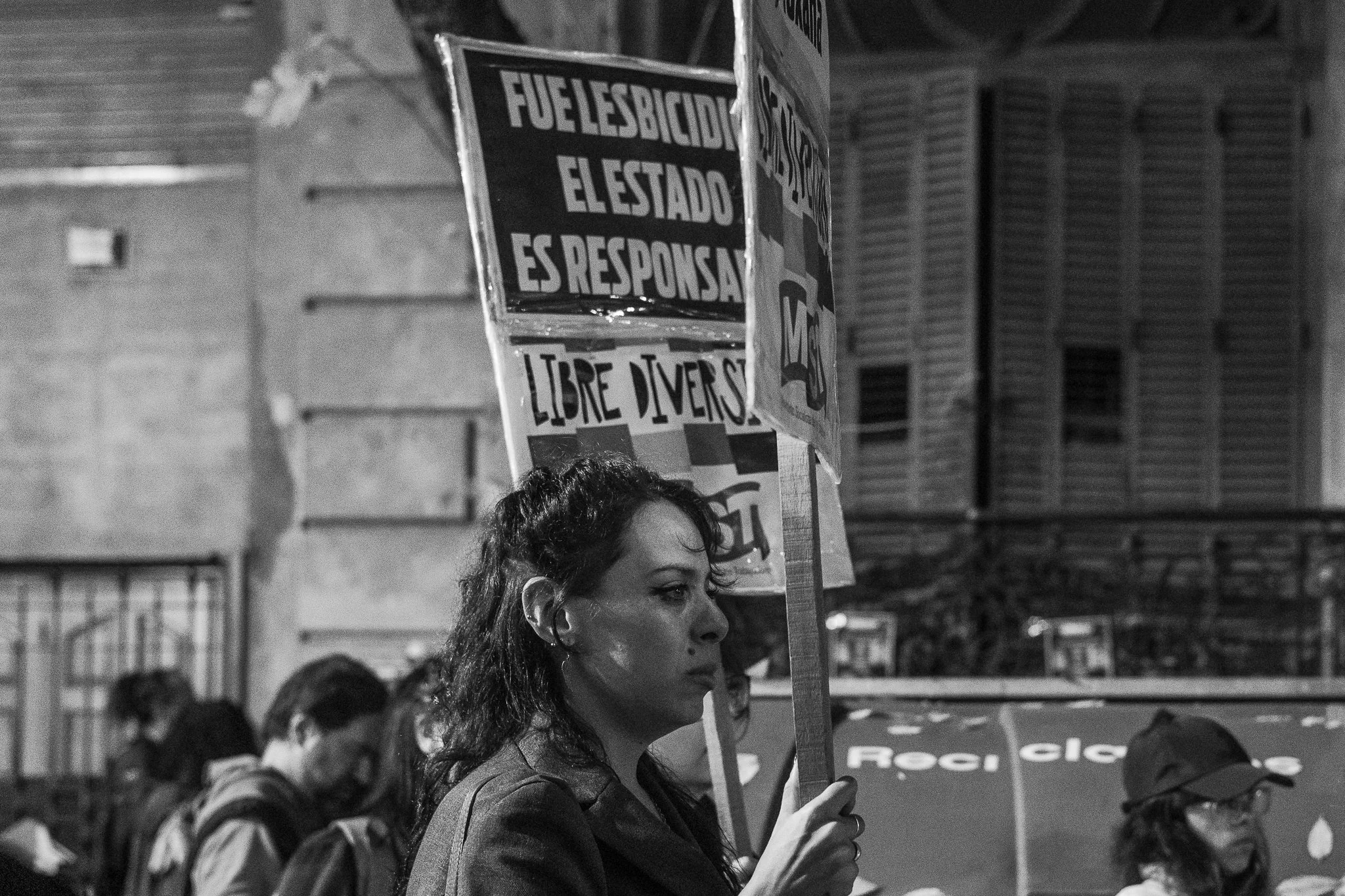 Mujer participando en una manifestación, sosteniendo un cartel que dice 'libre diversidad' a la noche, con otras personas presentes en el fondo.
