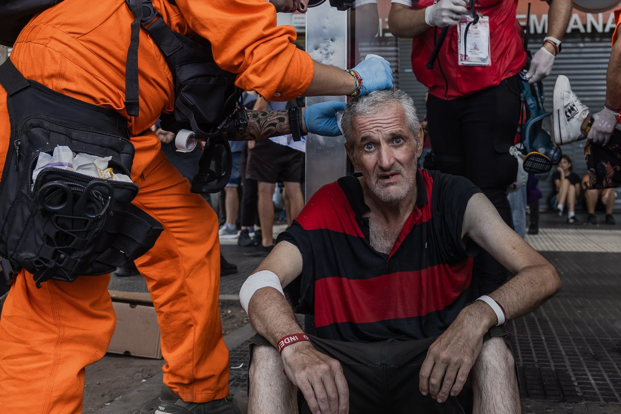 Persona recibiendo atención médica de un equipo de rescate en una marcha o competencia, sentado en el suelo con un vendaje en el brazo y expresión preocupada.