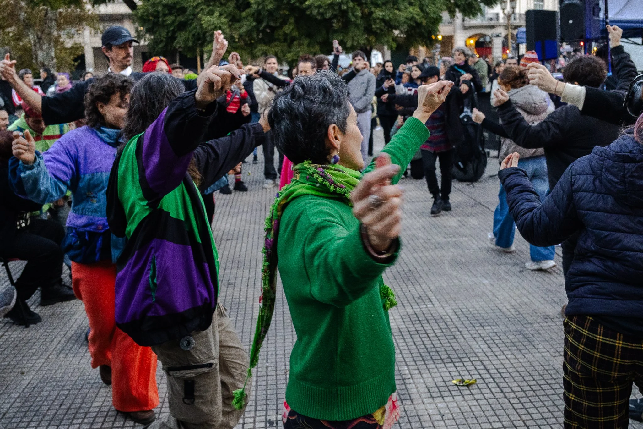 Grupo de personas bailando en una reunión al aire libre con edificios al fondo.