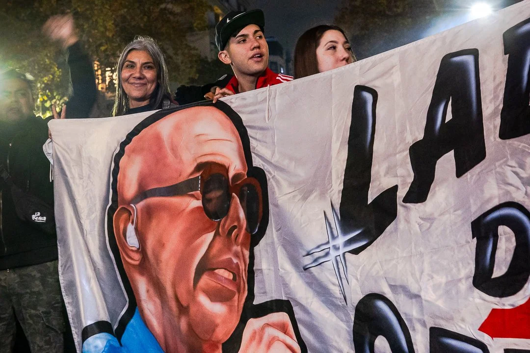 Personas sosteniendo una bandera gigante con la cara del Indio Solari: un hombre con gafas oscuras.