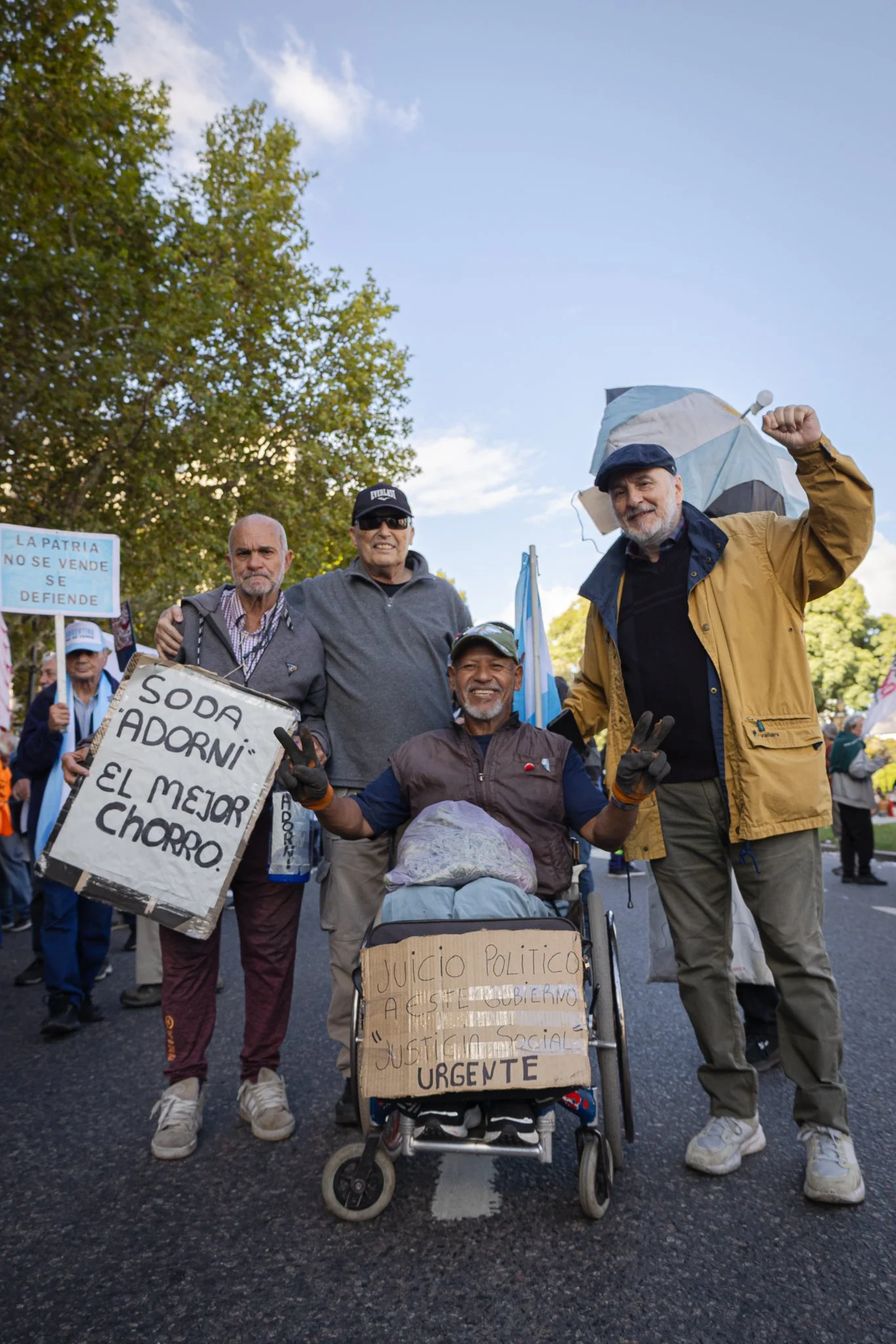 Grupo de personas en una manifestación, algunas con carteles y otros con signos de protesta. Una persona en silla de ruedas lleva un cartel que dice 'Juicio político a este gobierno' y otros sostienen signos que dicen 'La patria no se vende, se defie