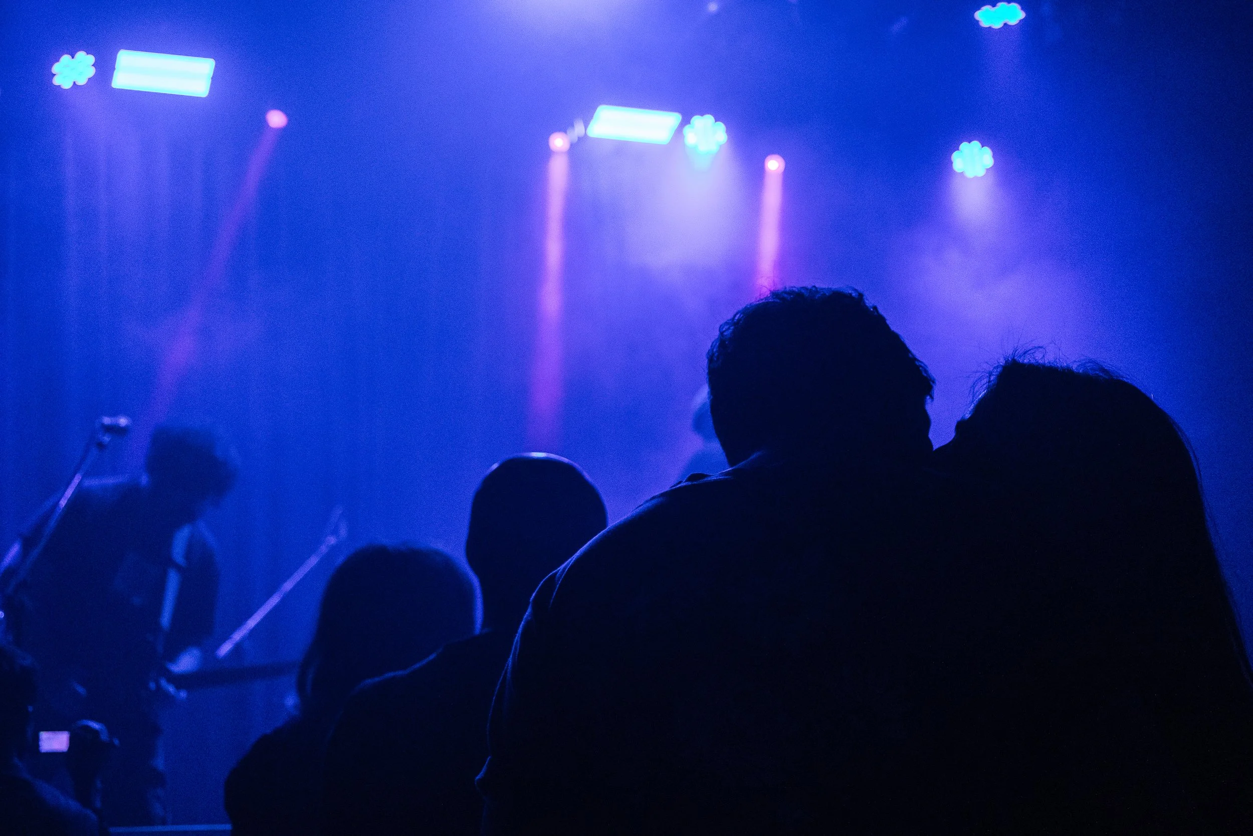 Personas en un escenario con luces azules, algunas se ven en silueta, parecen estar en un concierto o evento nocturno.