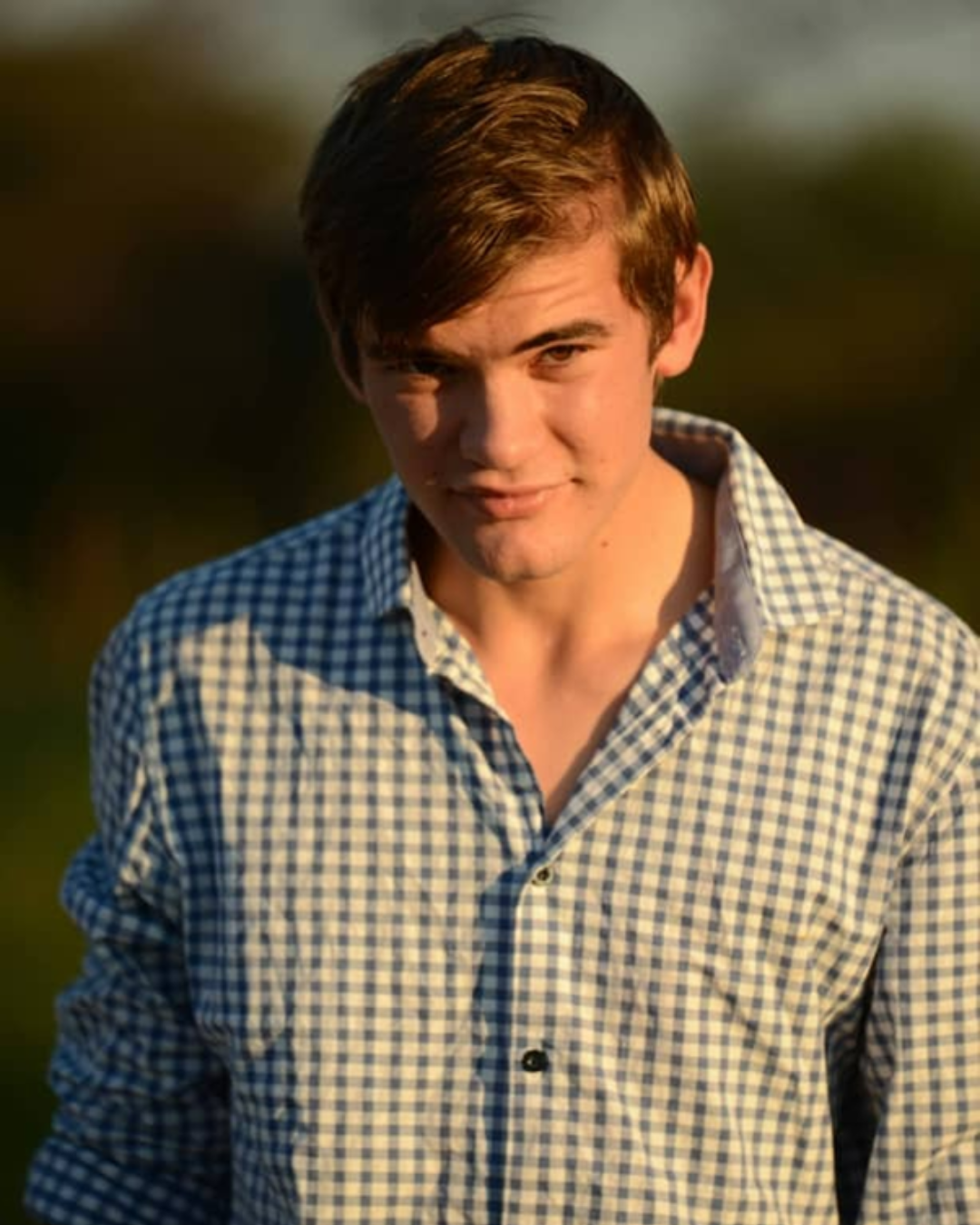 A young man with brown hair outdoors during sunset.