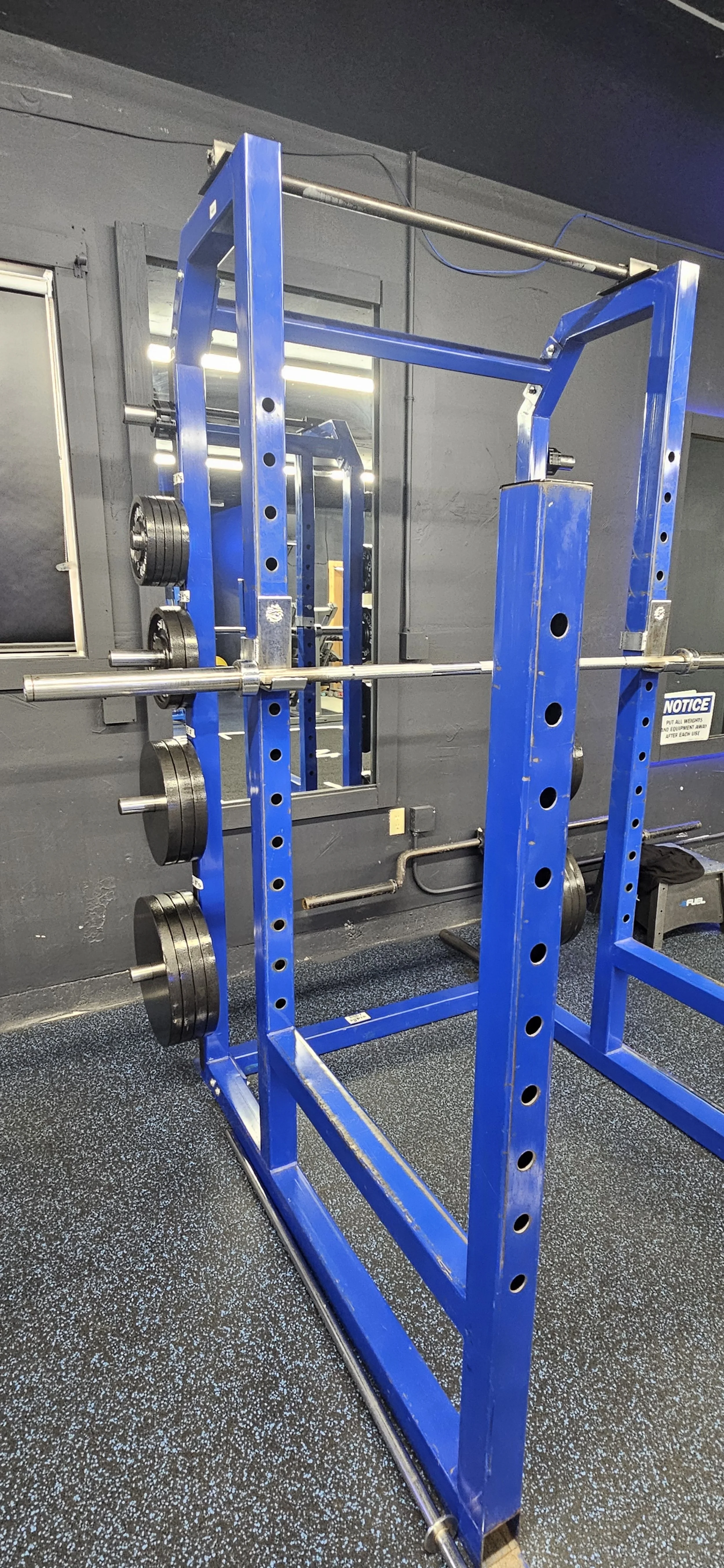 Blue power cage with barbell and weight plates in a gym.