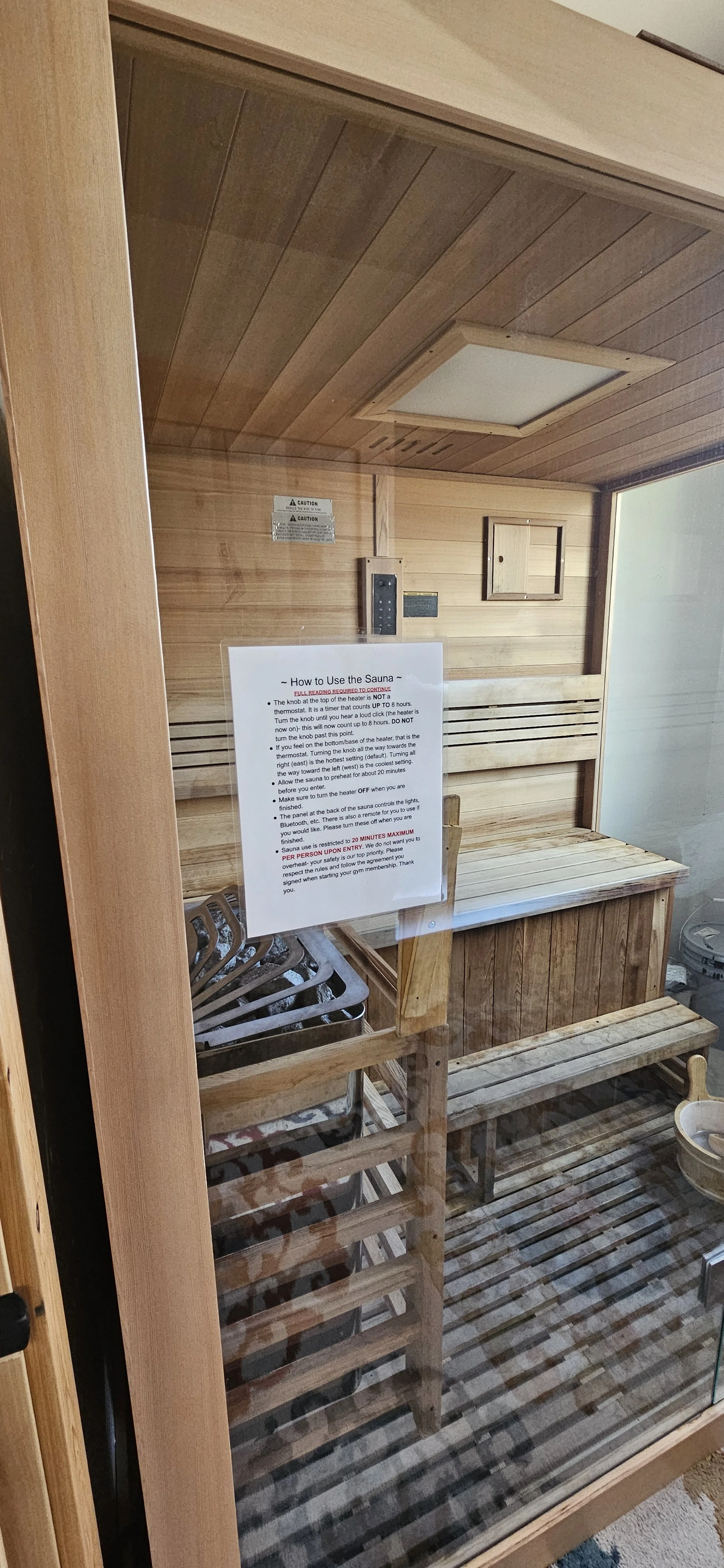 Inside a wooden sauna with a bench, a sign with instructions, and a heater. The sauna has a wooden door with a glass panel.