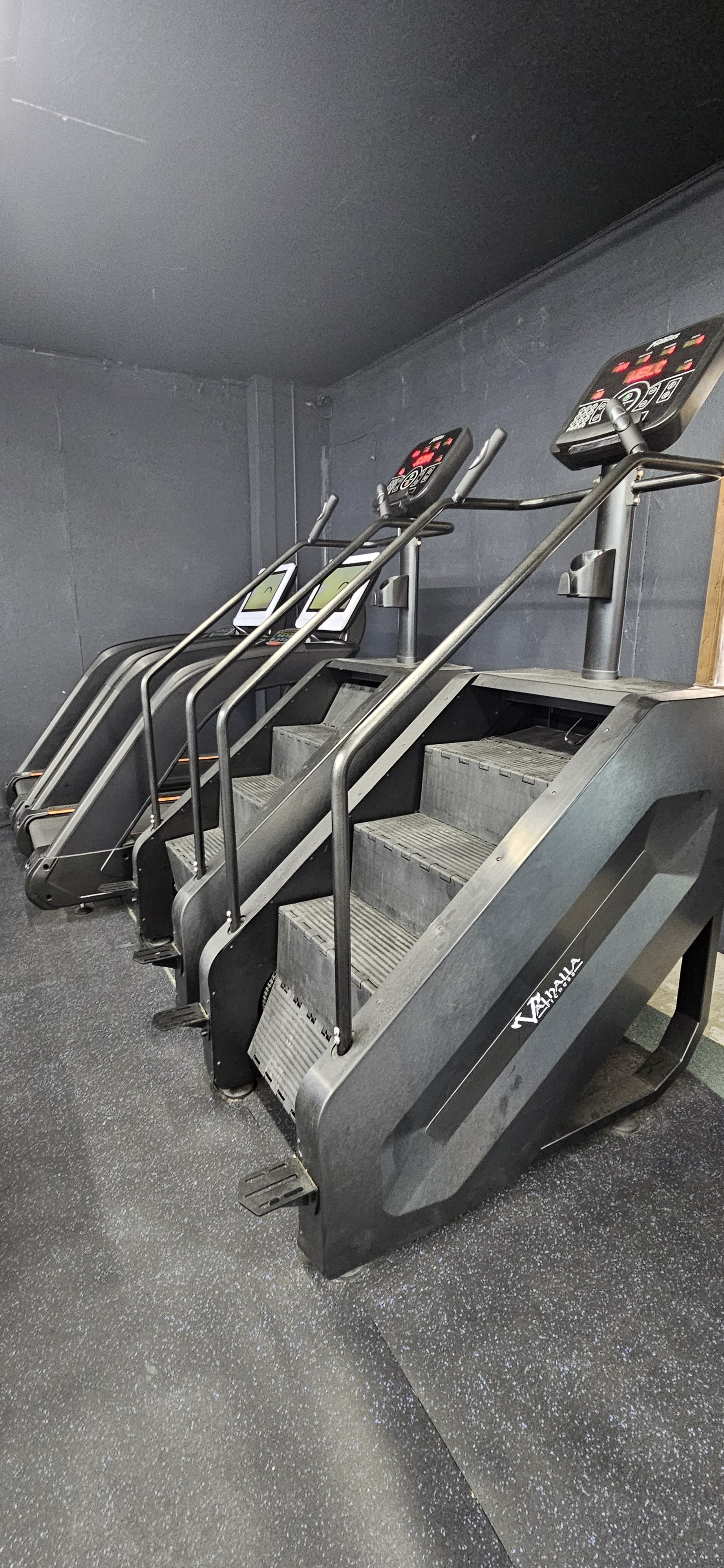 Three stair machines used for stepping or stair climbing exercise in a gym, with digital display screens on top.