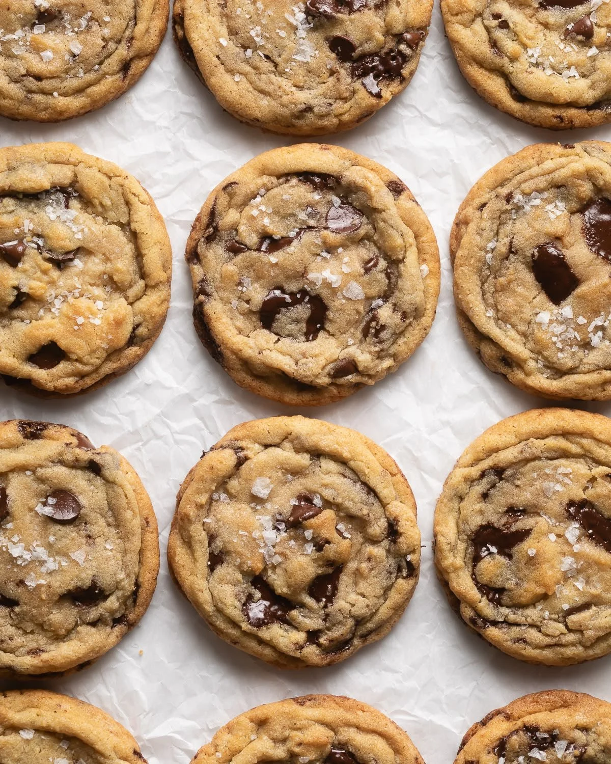 A close-up of chocolate chip cookies sprinkled with sea salt on parchment paper.