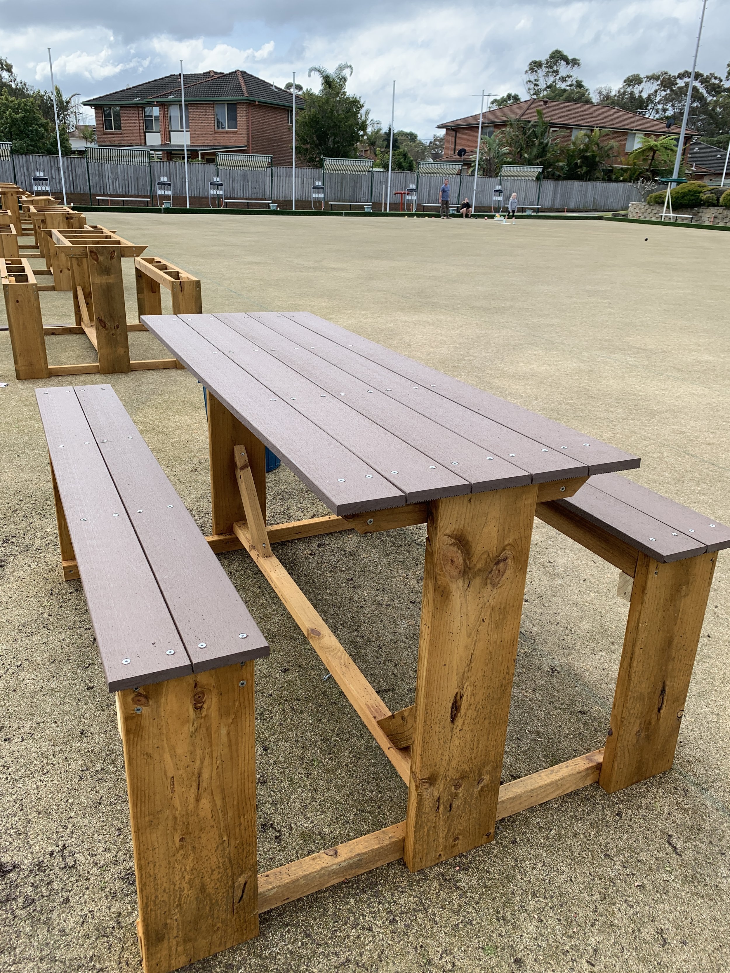 Empty wooden picnic table and benches on a sports field in a suburban neighborhood.