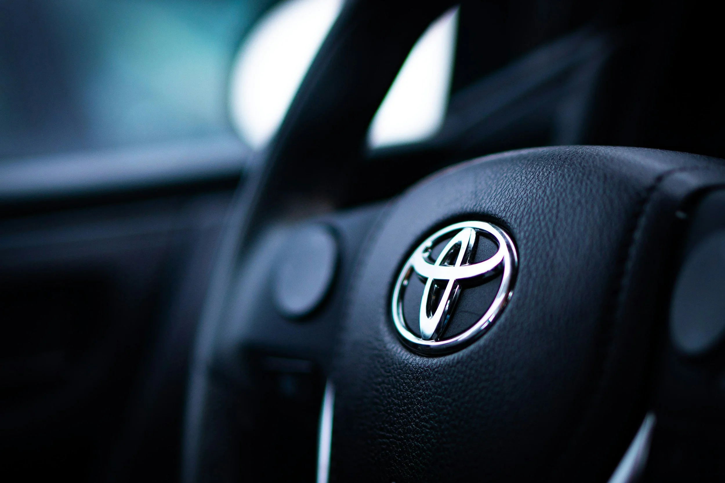 Close-up of a black Toyota car steering wheel with a silver Toyota emblem at the center.