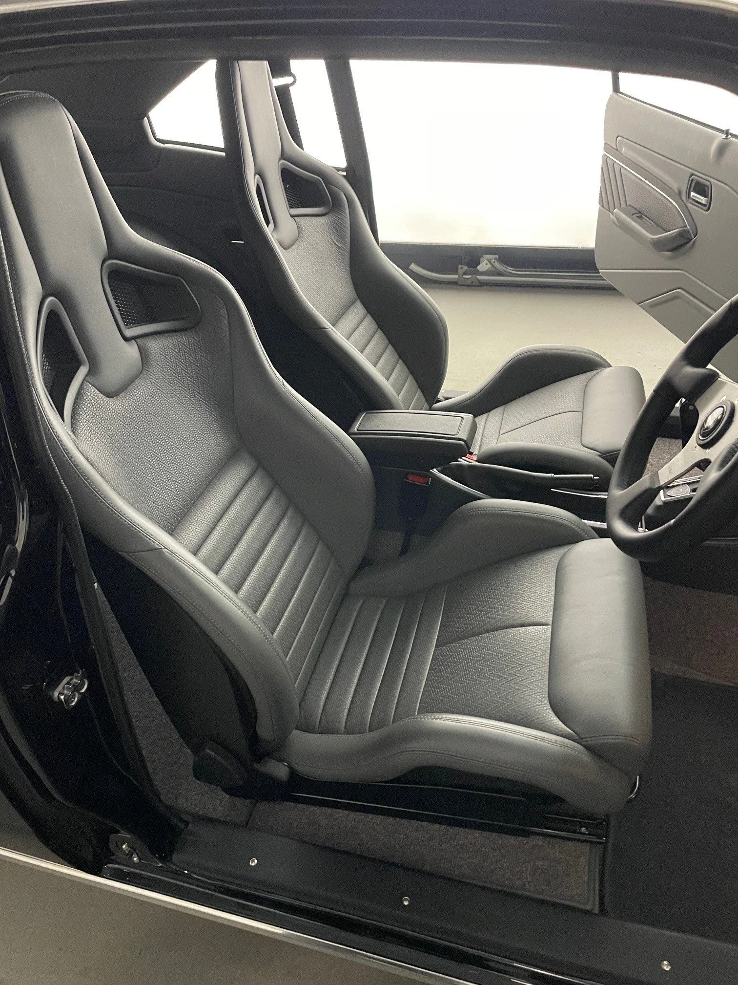 Autoprep Sydney Car Detailing - Interior view of the cockpit of a sports car with two black racing-style bucket seats, a steering wheel, and a side window.