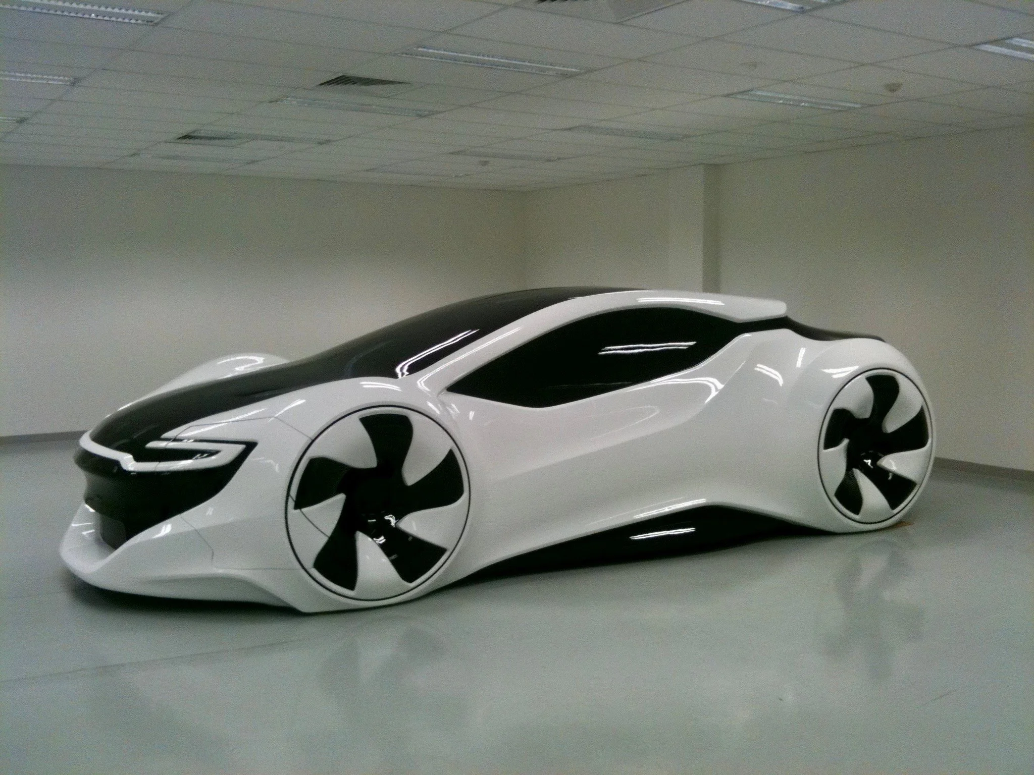 Futuristic concept car with aerodynamic black and white body, displayed indoors with glossy floor and ceiling lights.