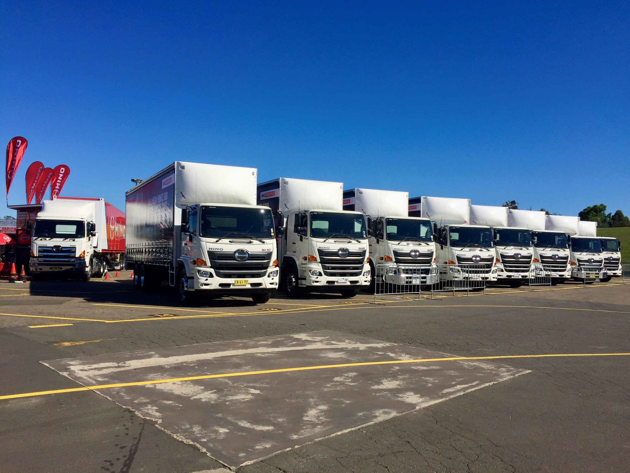 Multiple white delivery trucks parked in a lot on a clear, sunny day with a blue sky.