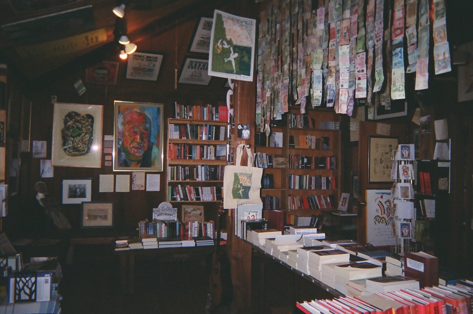 Elana Kline Art Photography: Interior of a bookstore or library filled with wooden bookshelves, artwork, and hanging currency notes on the wall.