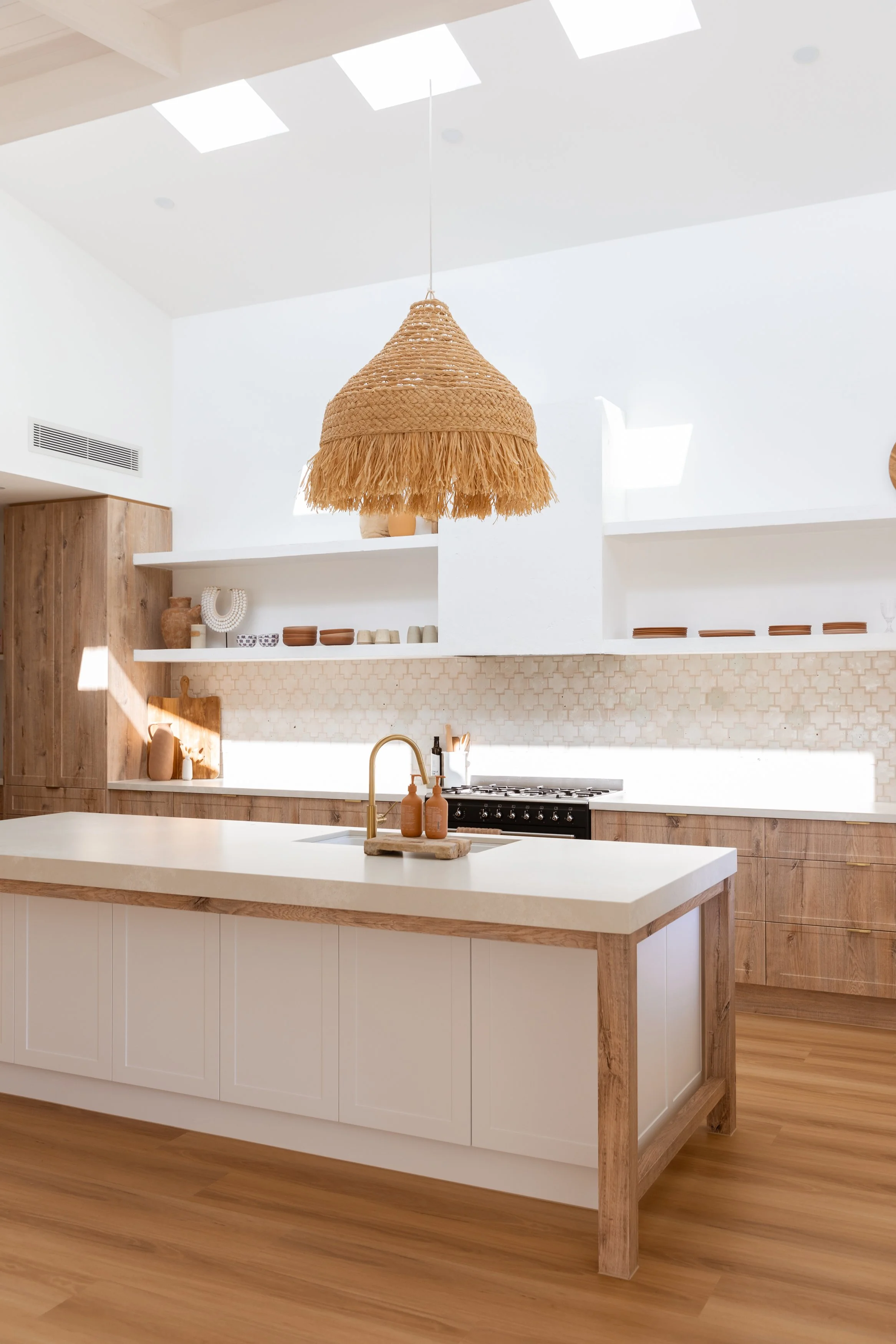 Bright modern kitchen with white island, wooden cabinets, open shelves, and a woven pendant light