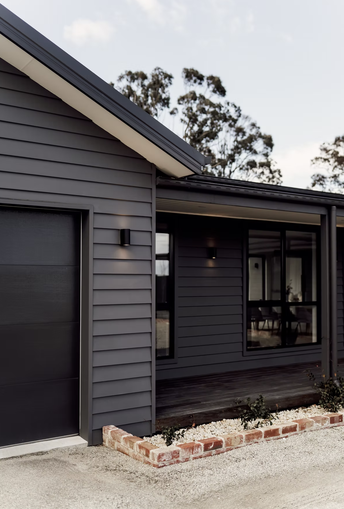 Modern house with dark gray siding, large glass windows, and a small front porch with brick edging and plants.