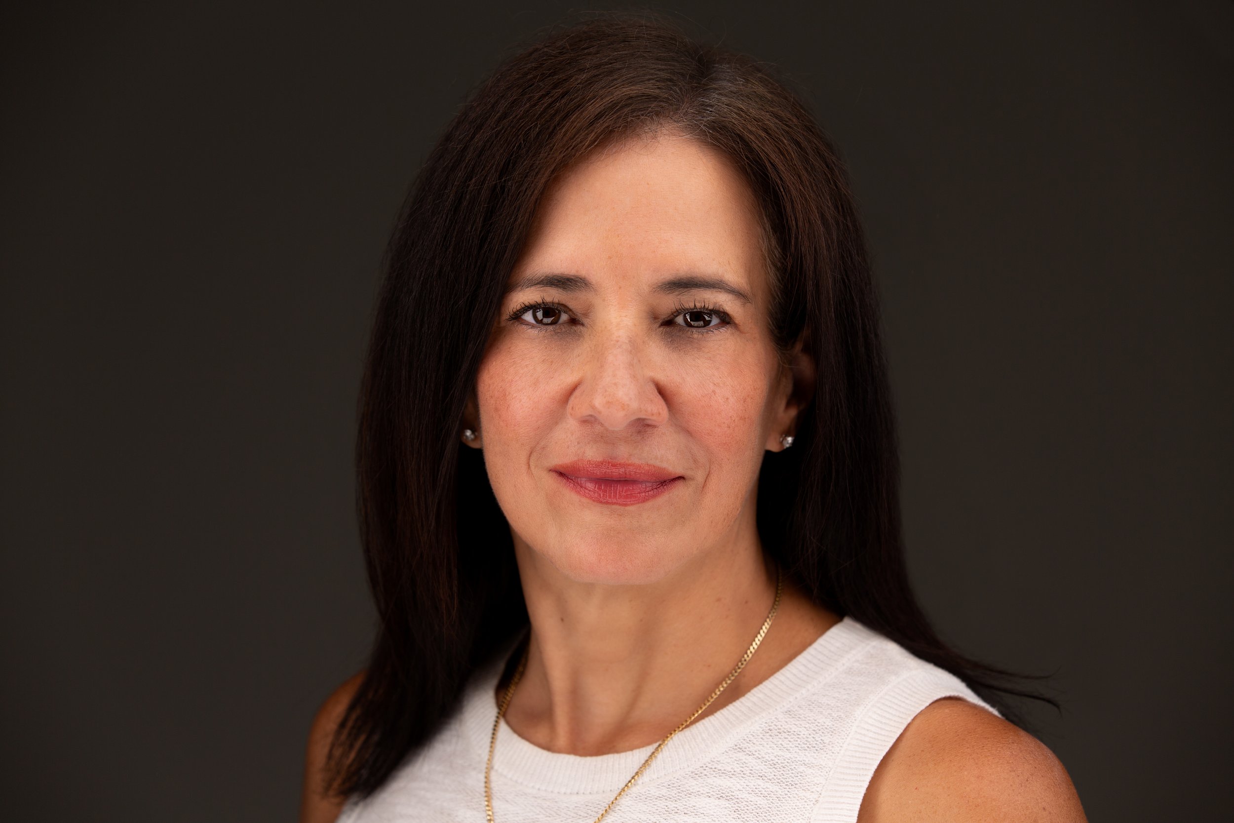 Picture of Ana Pedraza wearing a white knot top with a slight smile