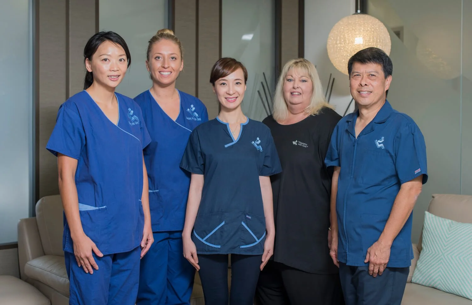 Group of five healthcare professionals, four women and one man, in scrubs and uniforms, standing in an office or medical facility.