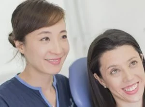 A dental professional smiling next to a woman smiling in a dental chair.