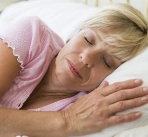 A woman sleeping peacefully on her side with her eyes closed, resting her head on a pillow.