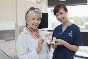 A young female healthcare worker assisting an elderly woman with a blood test in a clinical setting.