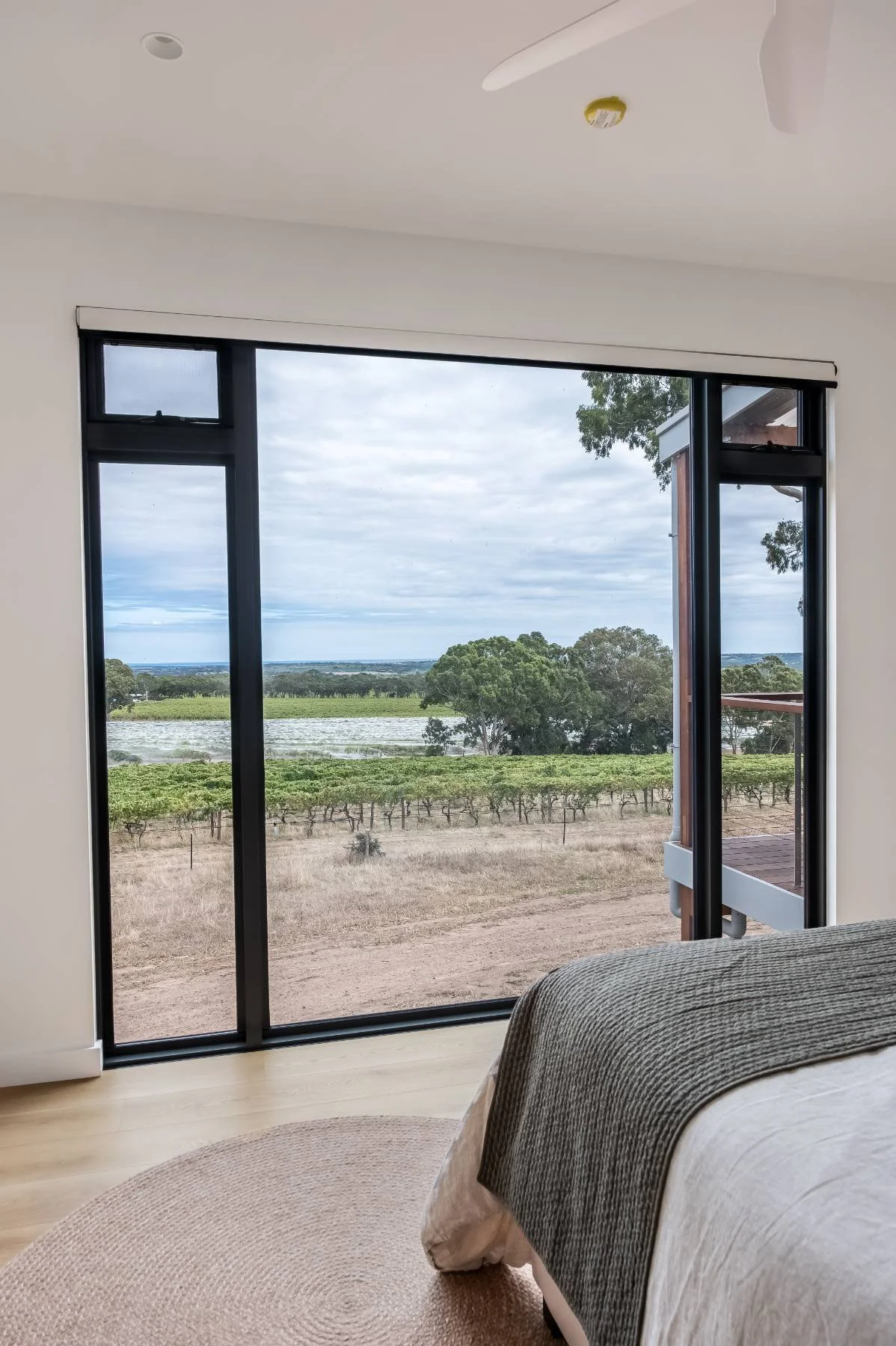 Interior view of a bedroom with a large sliding glass door overlooking a farm or vineyard landscape with trees and fields.