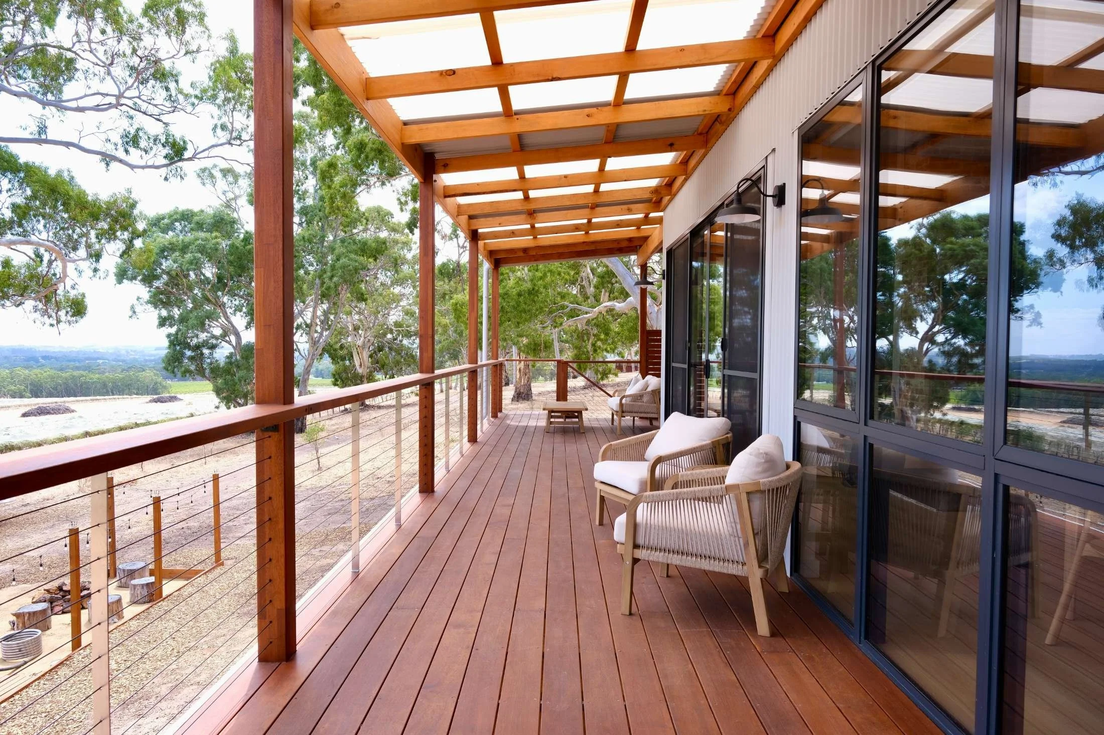 Wooden porch with railing and outdoor seating, overlooking trees and a distant landscape.