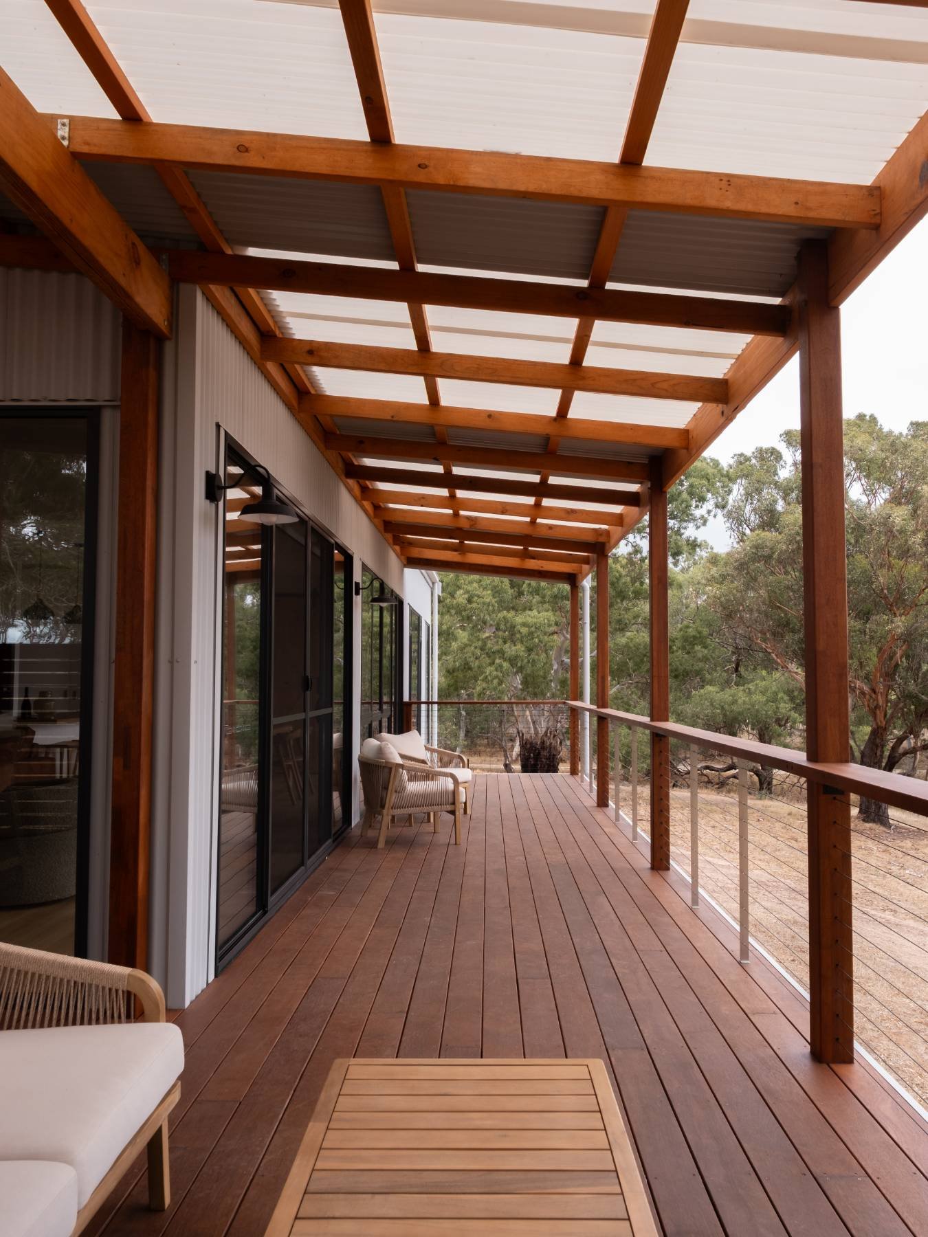 Wooden porch with chairs and a railing, overlooking a natural landscape with trees.