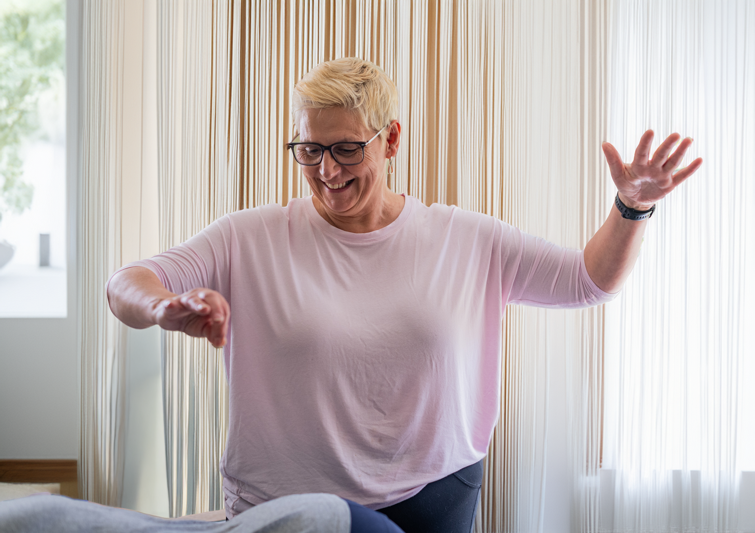 Owner, Marie with short blonde hair and glasses smiling and performing spinal energetics on a client