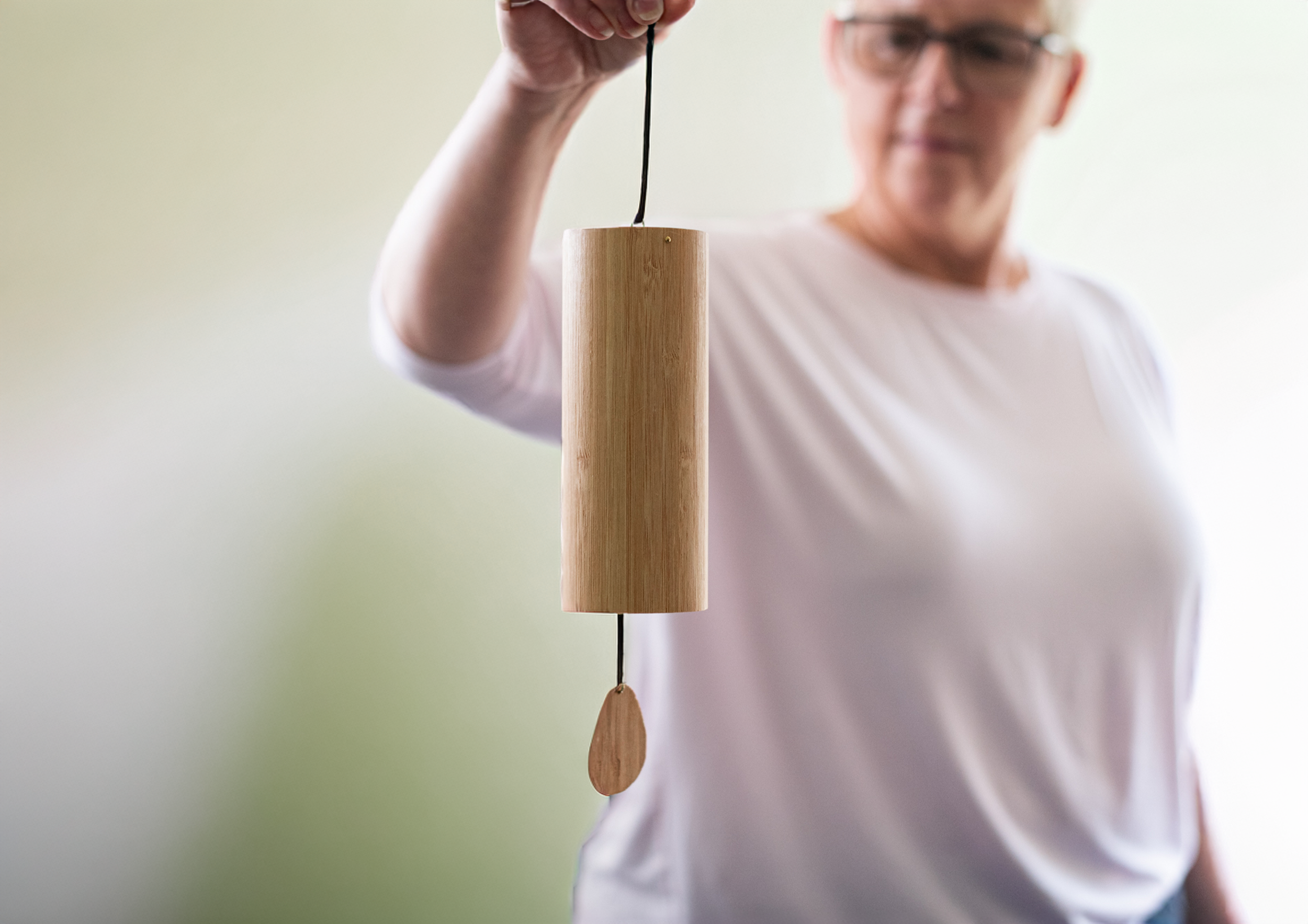 Owner, Marie wearing glasses and a white shirt holding a wooden pendulum with a teardrop-shaped weight, swinging from a black string while performing spinal energetics and Reiki