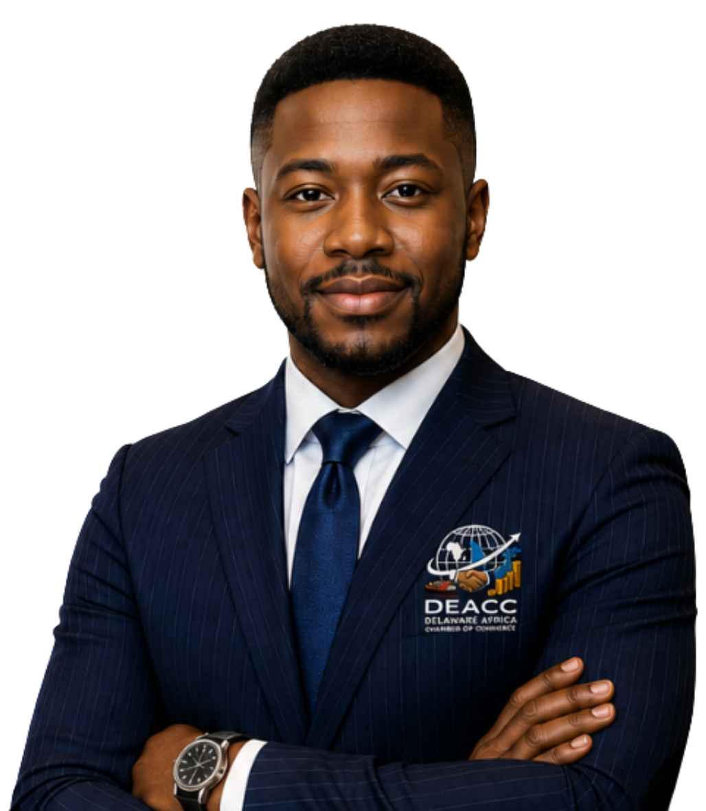 Portrait of a young African American man wearing a navy blue pinstripe suit, white shirt, and blue tie, with a DELAWARE ASIAN AMERICA CHAMBER OF COMMERCE (DEACC) logo on his suit jacket, smiling with arms crossed, standing against a black background.