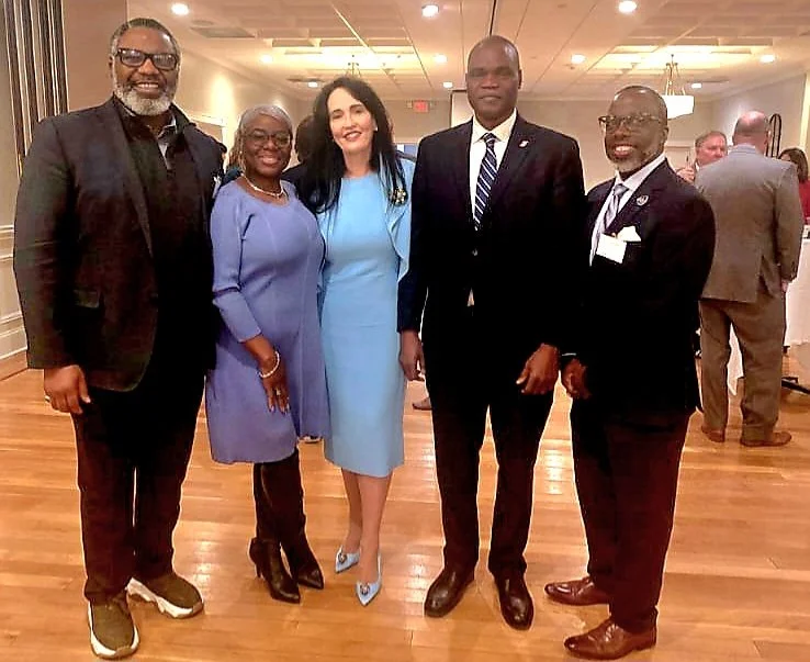 Group of five people in formal attire posing together indoors at a social event.